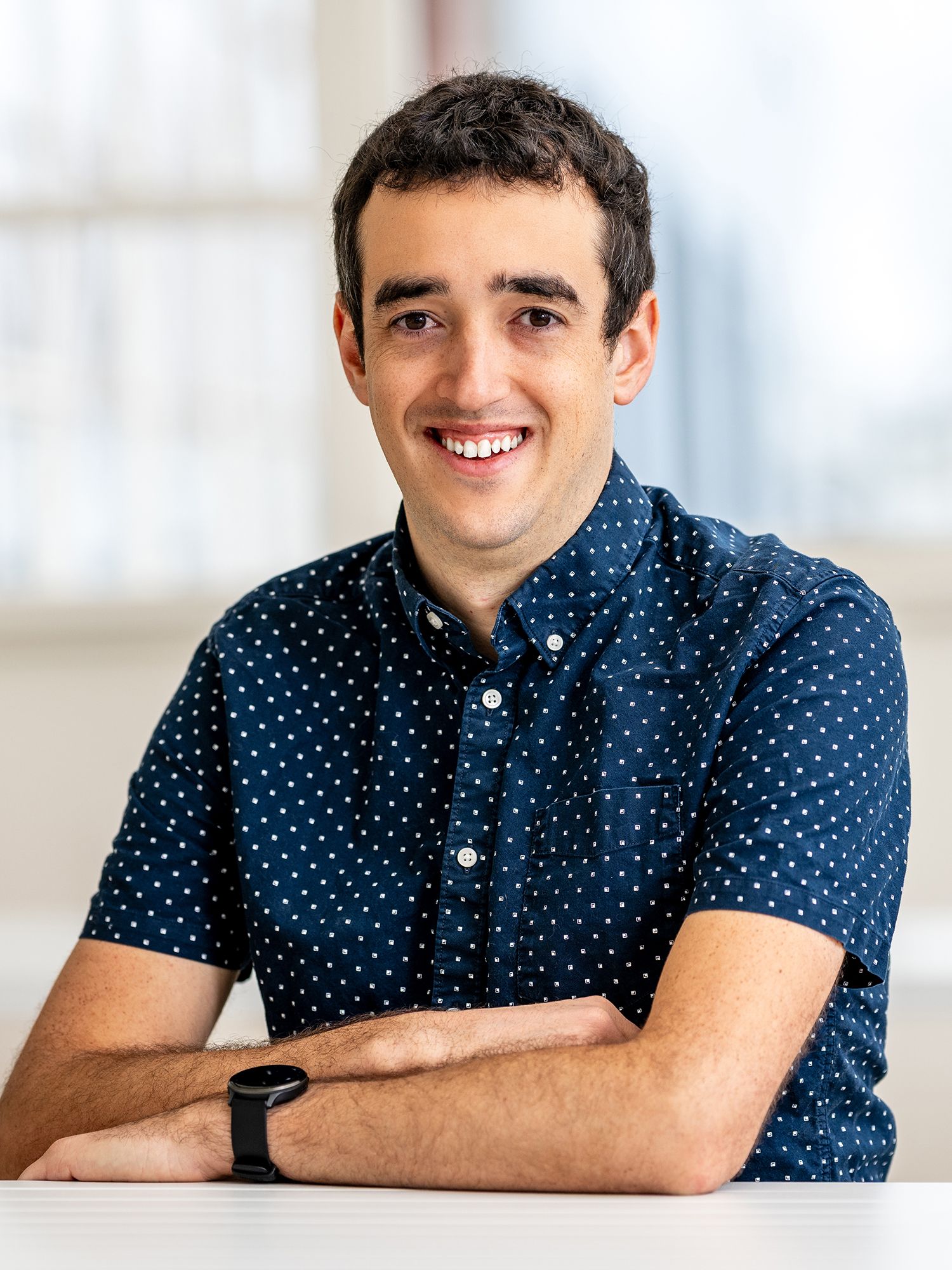 Smiling man in a patterned button-up shirt seated at a table