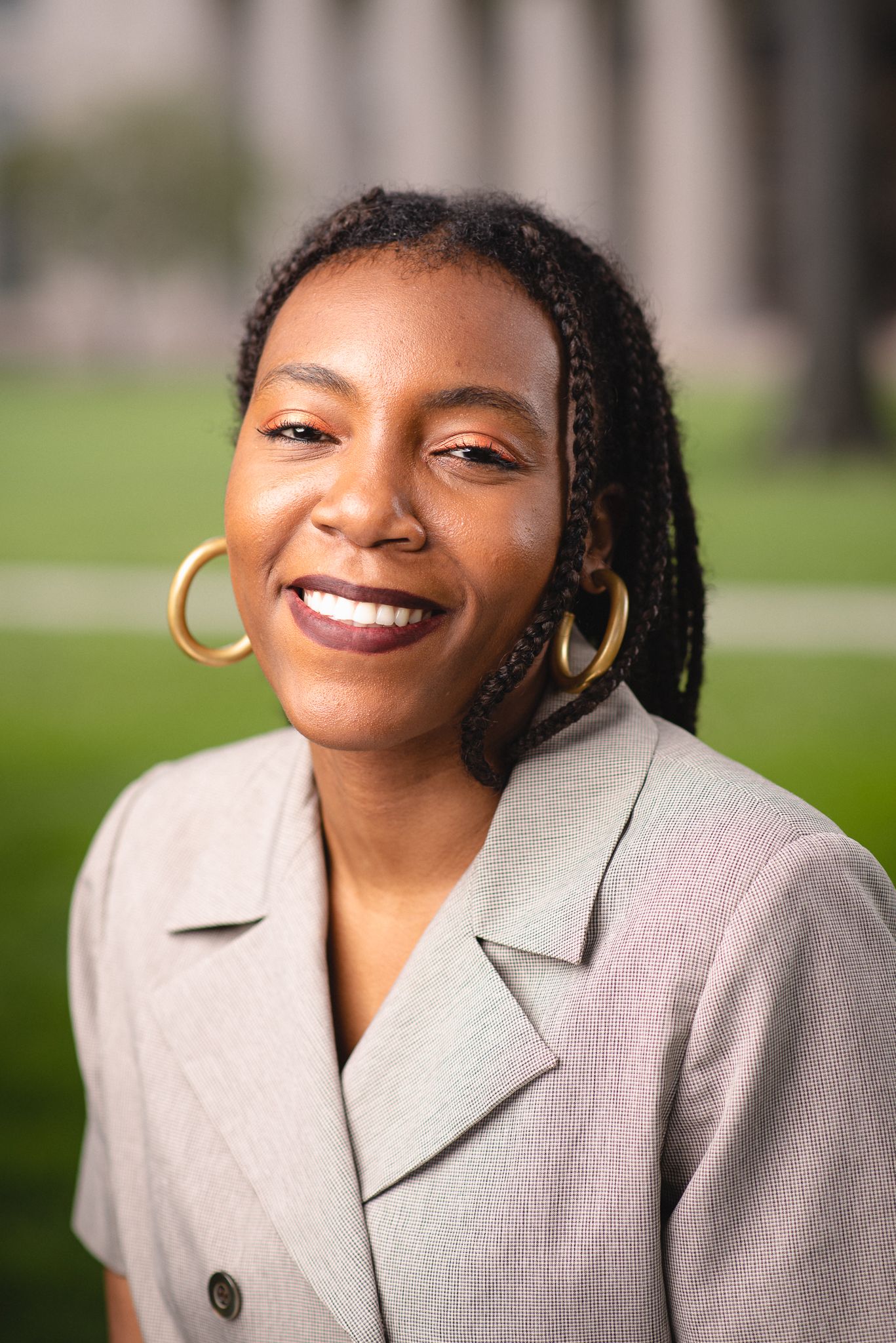 Woman with braided hair and hoop earrings smiling outdoors