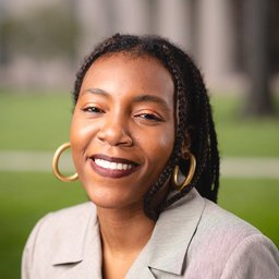 Woman with braided hair and hoop earrings smiling outdoors