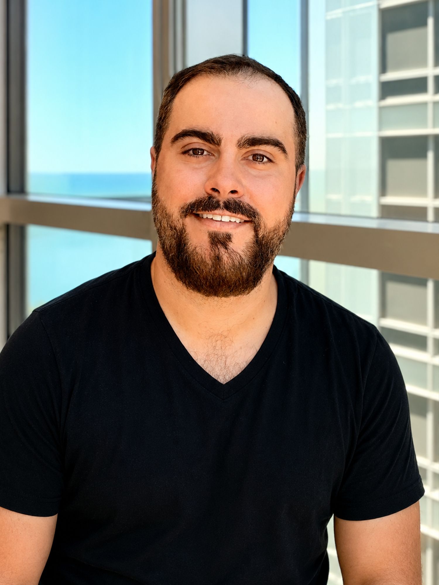 Bearded man smiling in front of office windows