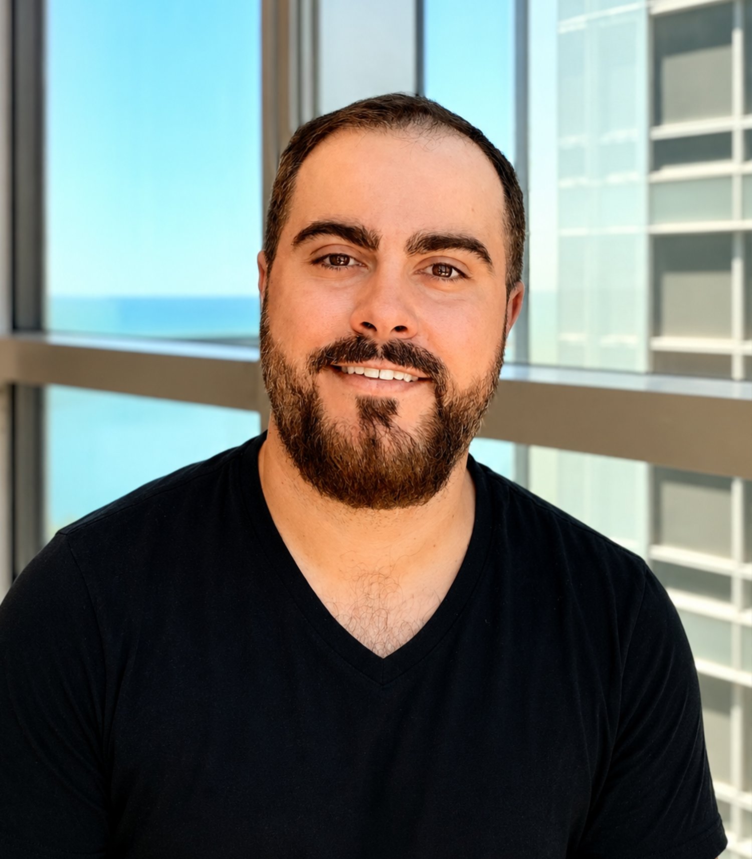 Bearded man smiling in front of office windows