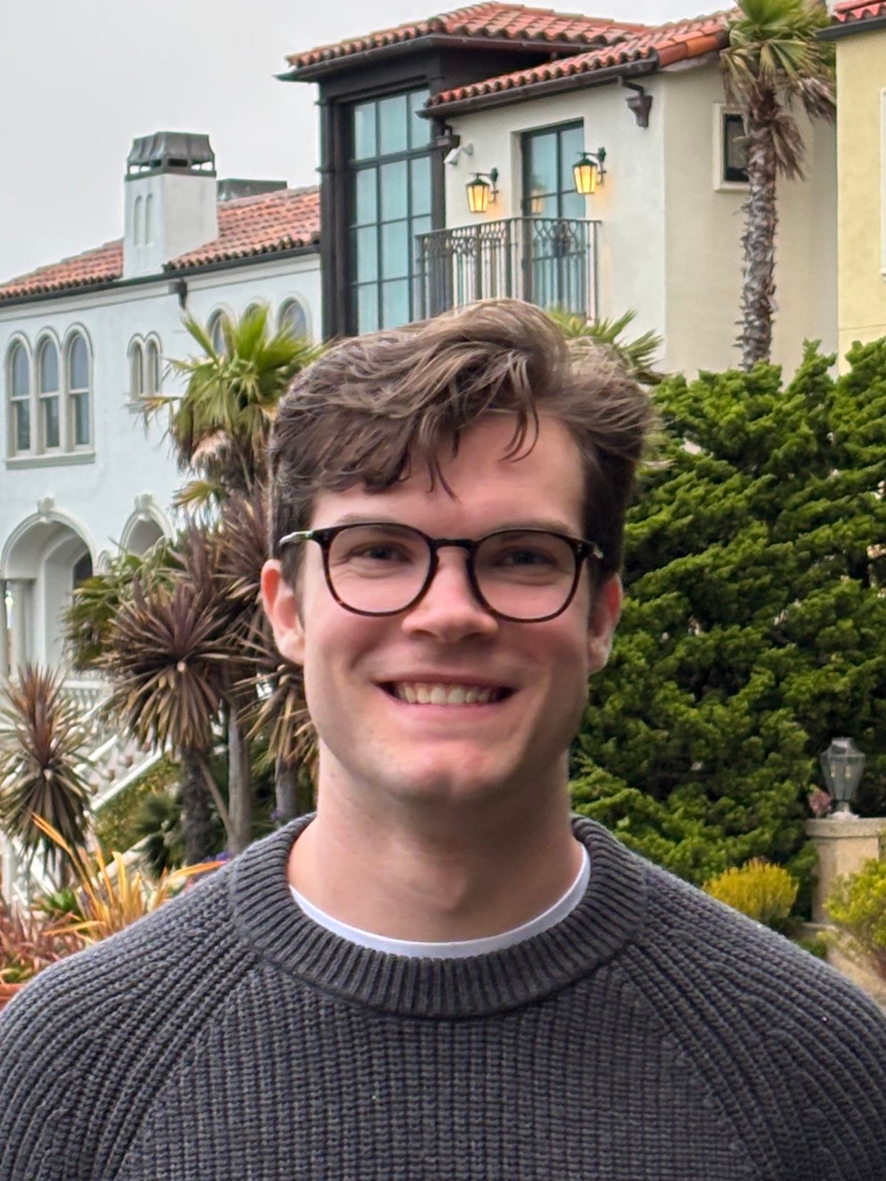 Smiling man wearing glasses and a sweater outdoors