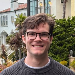 Smiling man wearing glasses and a sweater outdoors