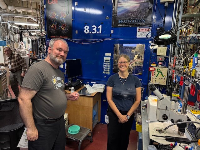 Two scientists stand beside laboratory equipment in a research facility