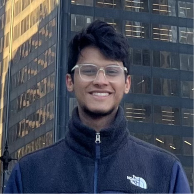 Smiling man wearing glasses stands in front of office buildings