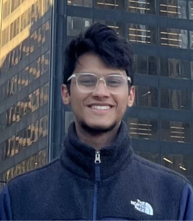Smiling man wearing glasses stands in front of office buildings