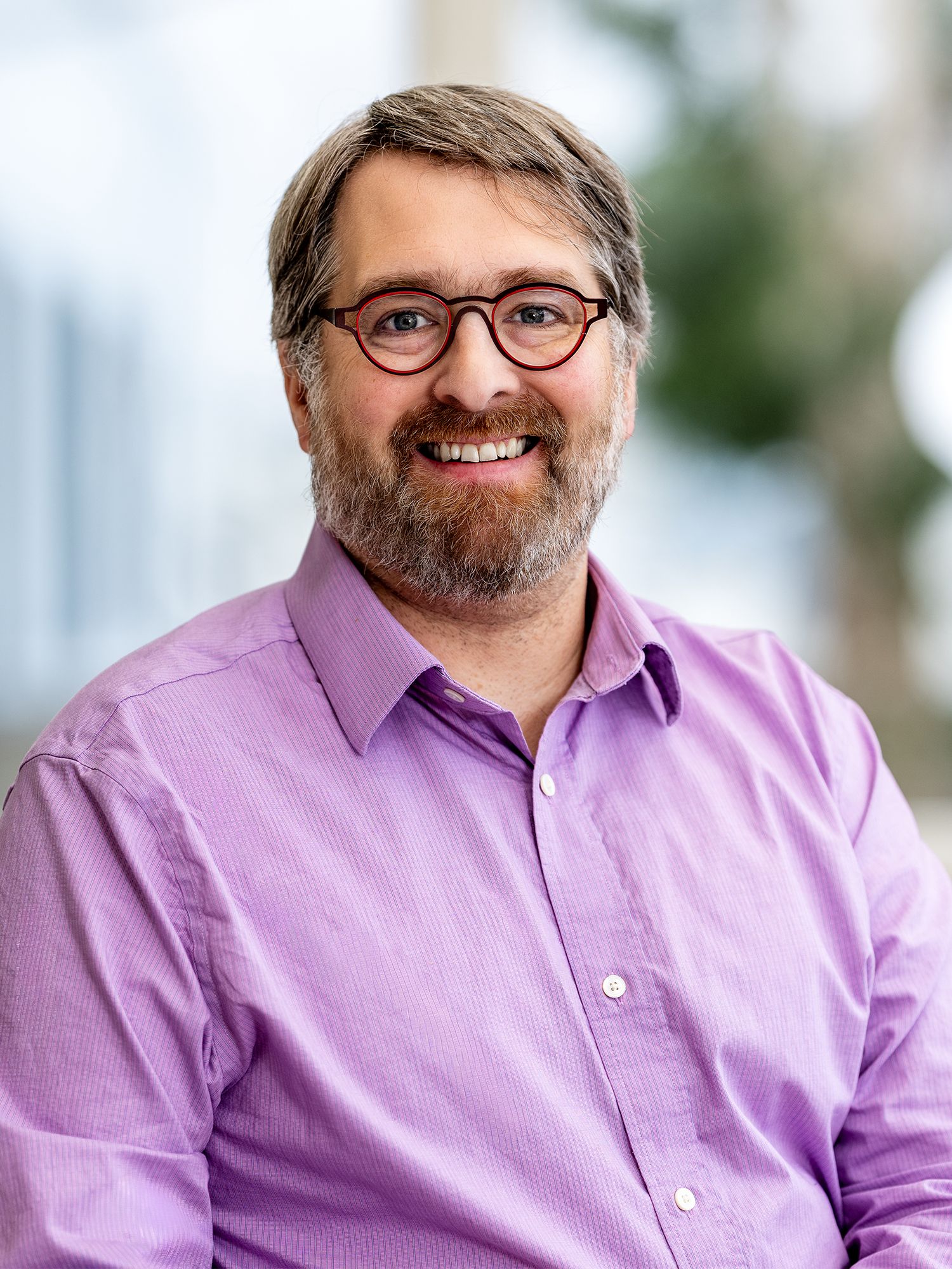 Smiling bearded man wearing round glasses and a collared shirt