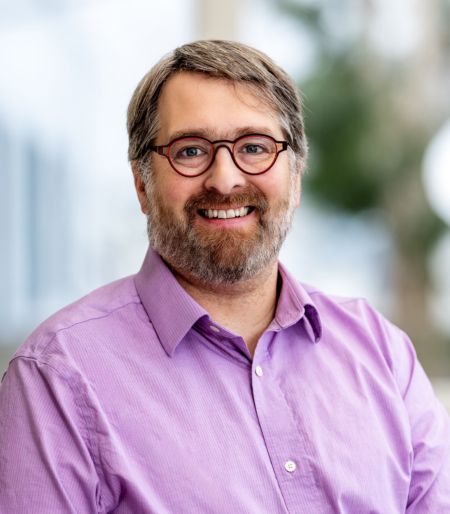 Smiling bearded man wearing round glasses and a collared shirt