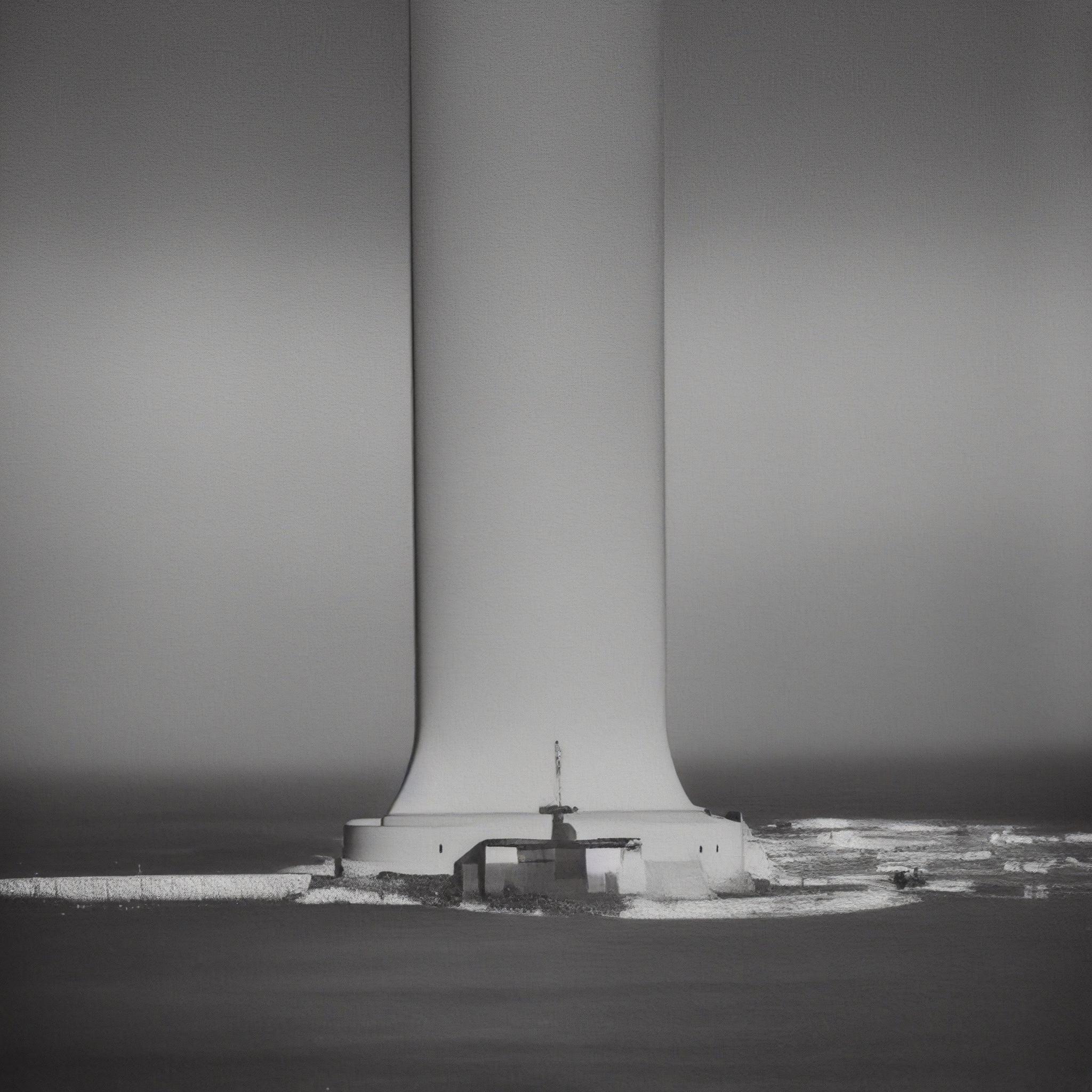 A lighthouse on a rocky coast dwarfed by three massive wind-turbine towers rising into fog.