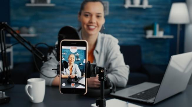 Content creator recording a video for social media using a smartphone and laptop.