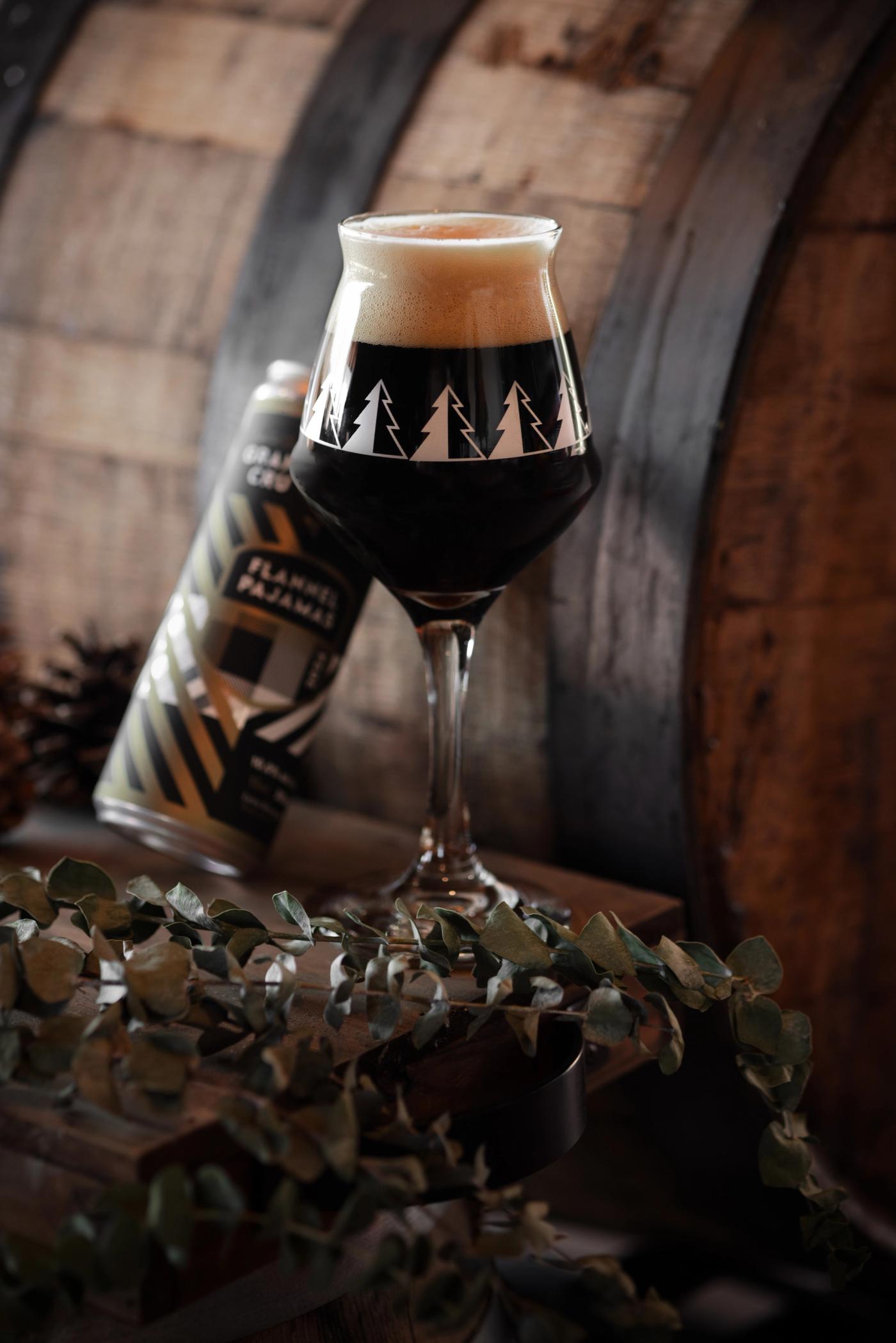 Camp Beer Co. Flannel Pajamas stout poured into a branded glass on an oak barrel