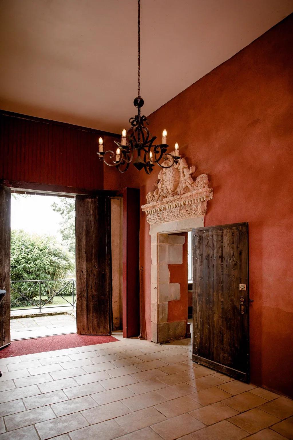 Le hall d'entrée aux murs rouges, sa porte sculptée ouverte sur le parc