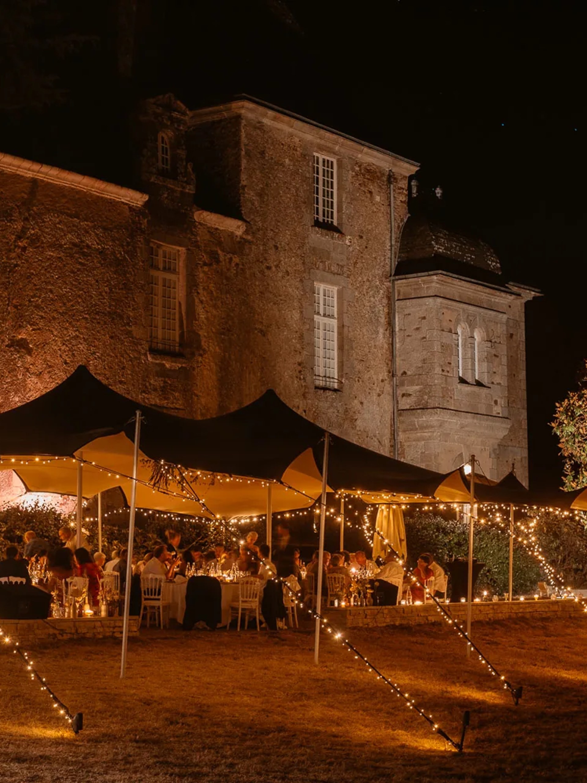 Dinner set outdoors under strings of lights, at nightfall