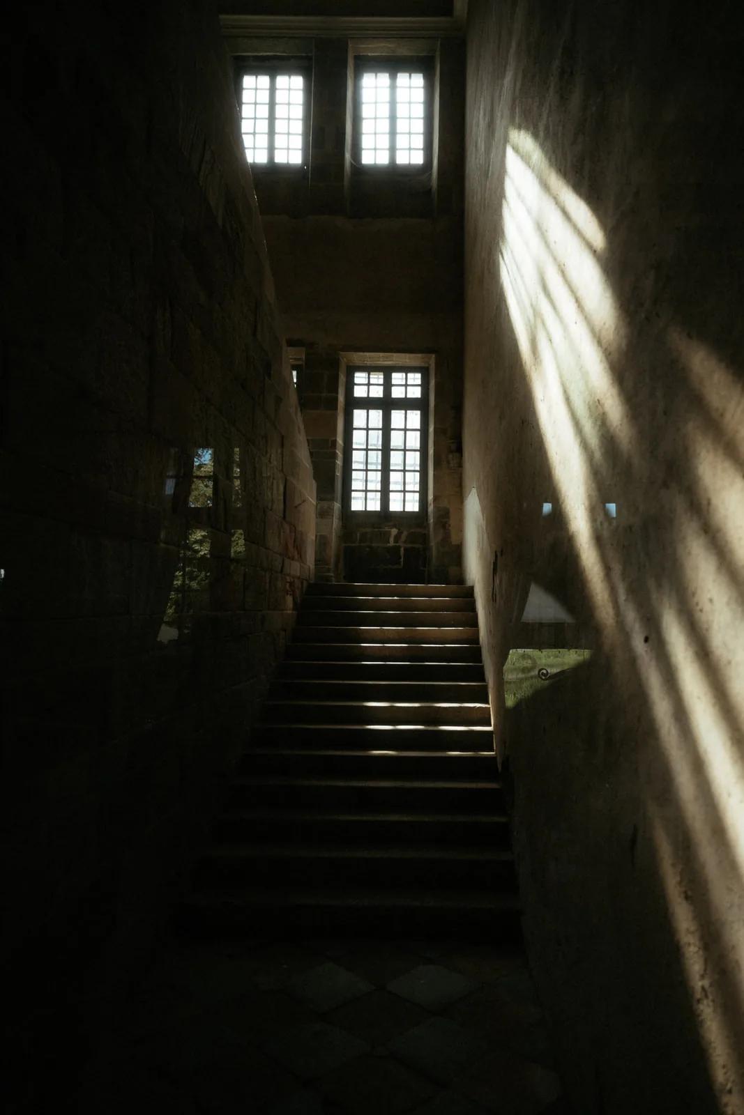 L'escalier de pierre du château, éclairé par une fenêtre à meneaux
