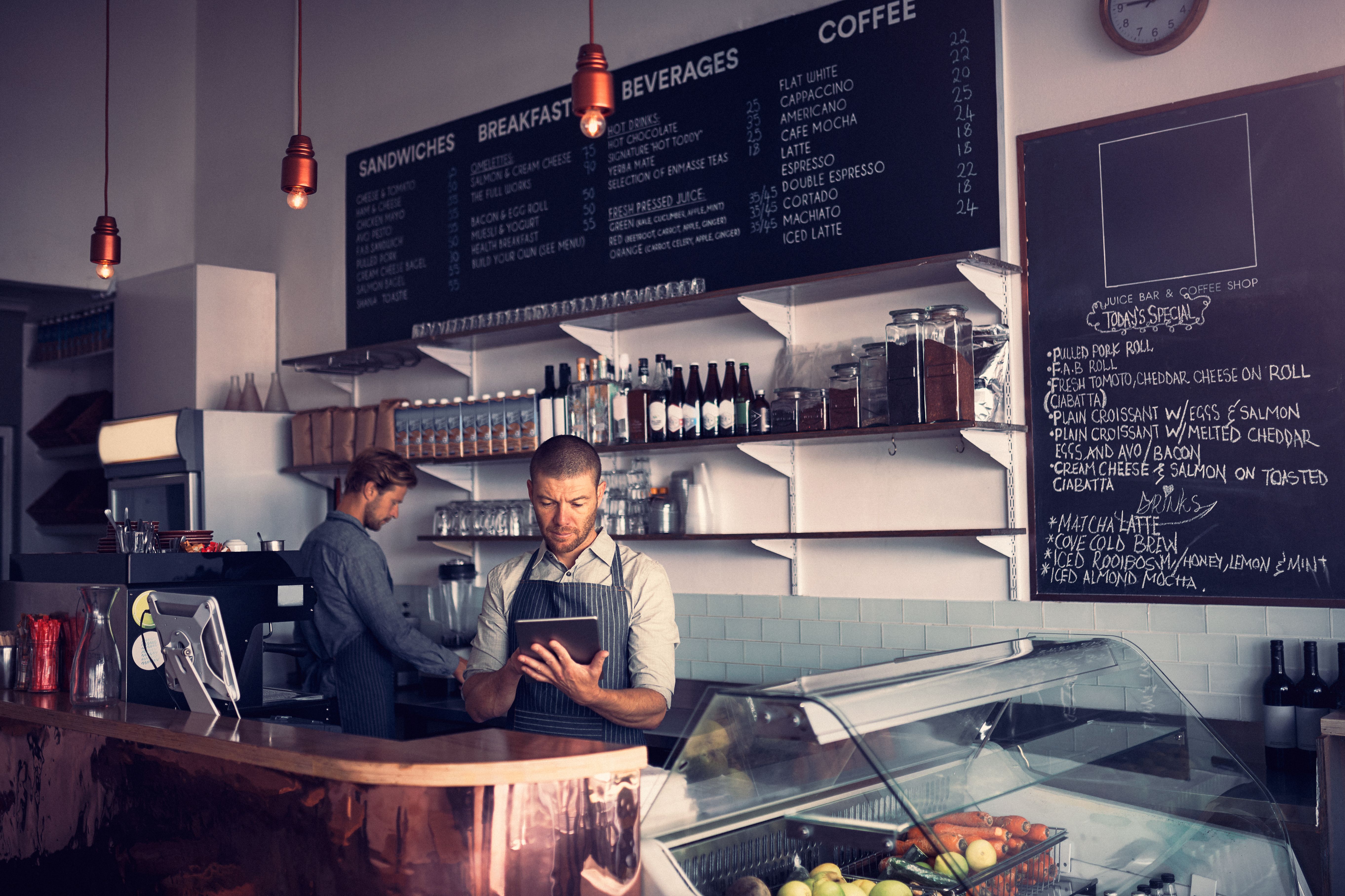 Staff behind the counter of a café, one checking orders on a tablet