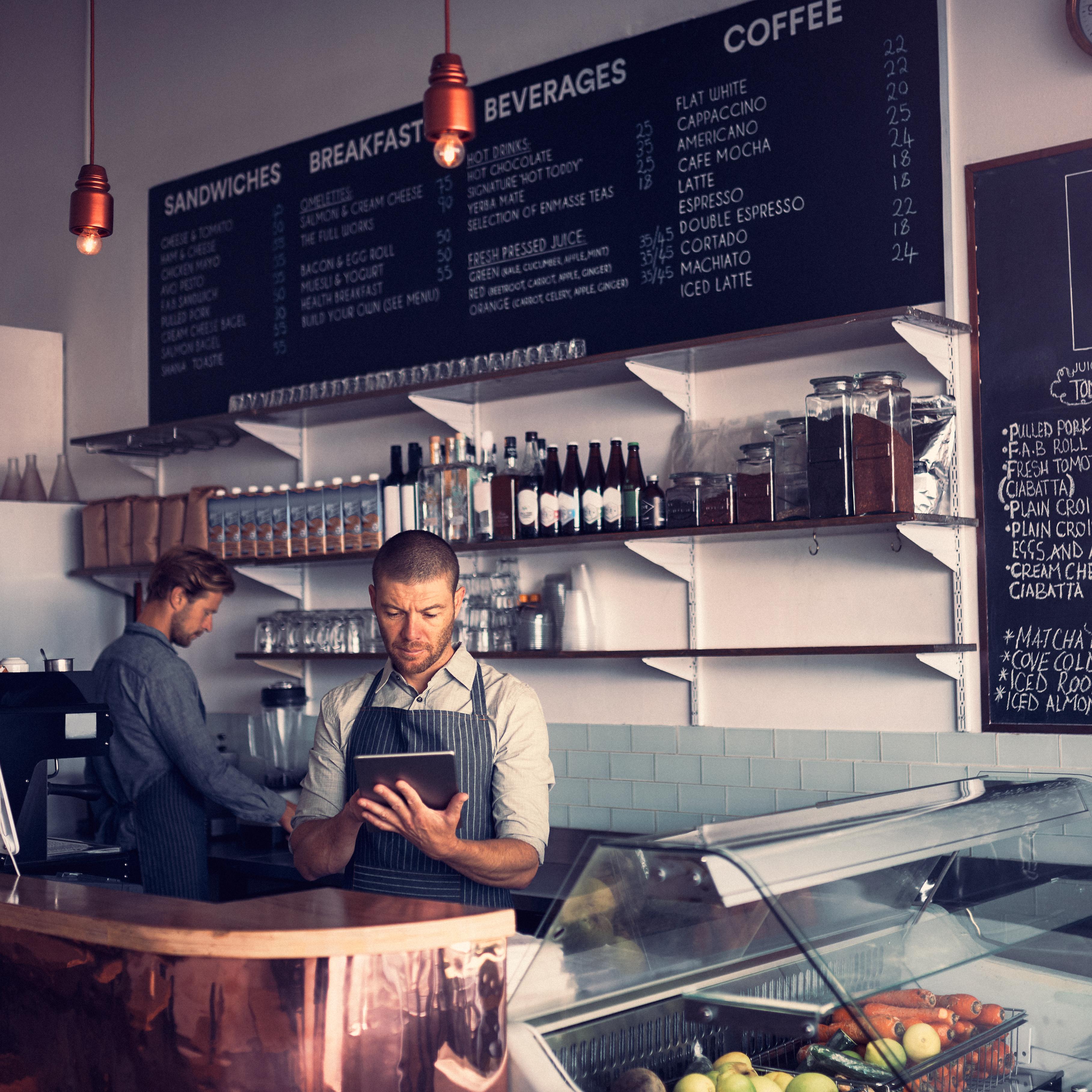 Staff behind the counter of a café, one checking orders on a tablet