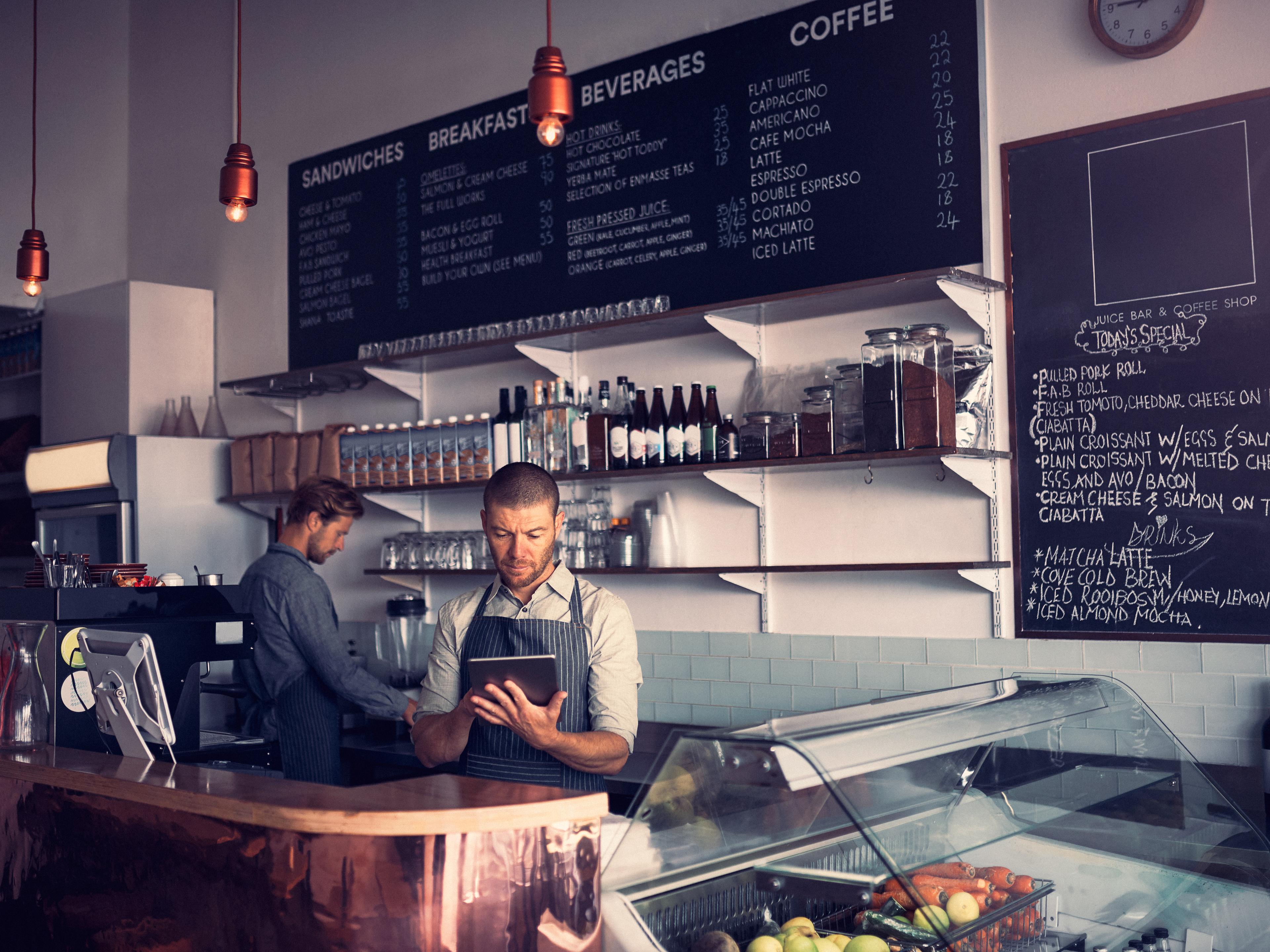 Staff behind the counter of a café, one checking orders on a tablet