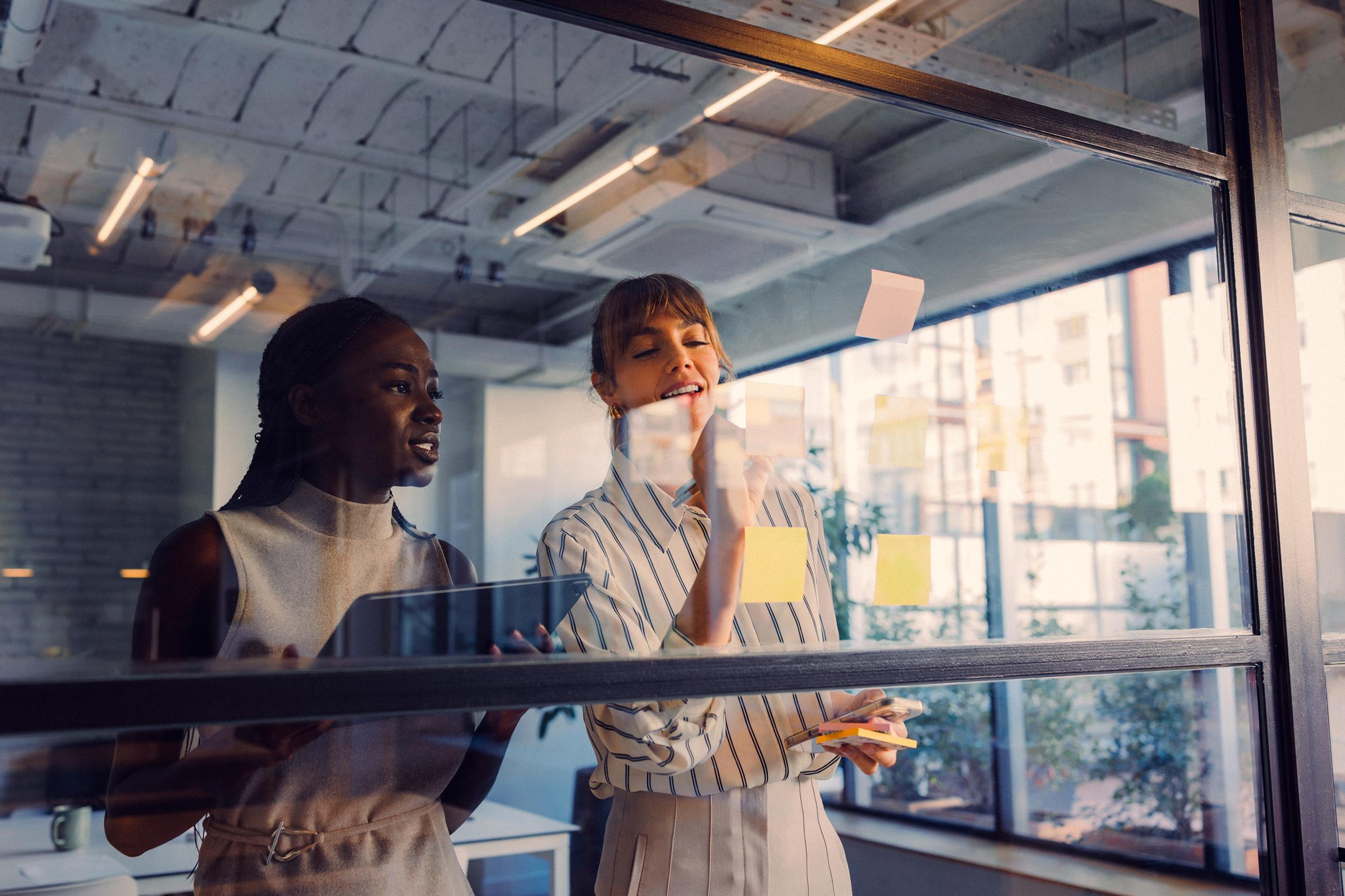 Two colleagues talking beside a glass wall covered in sticky notes