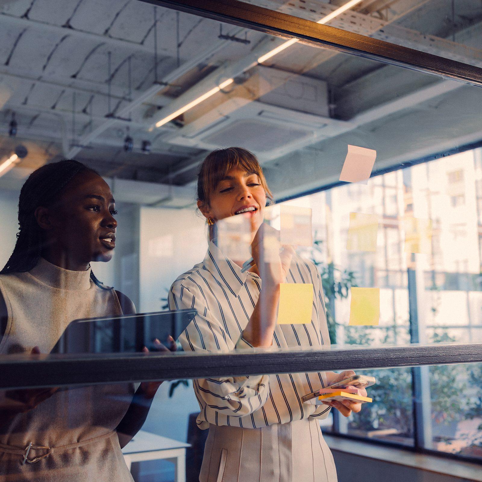 Two colleagues talking beside a glass wall covered in sticky notes