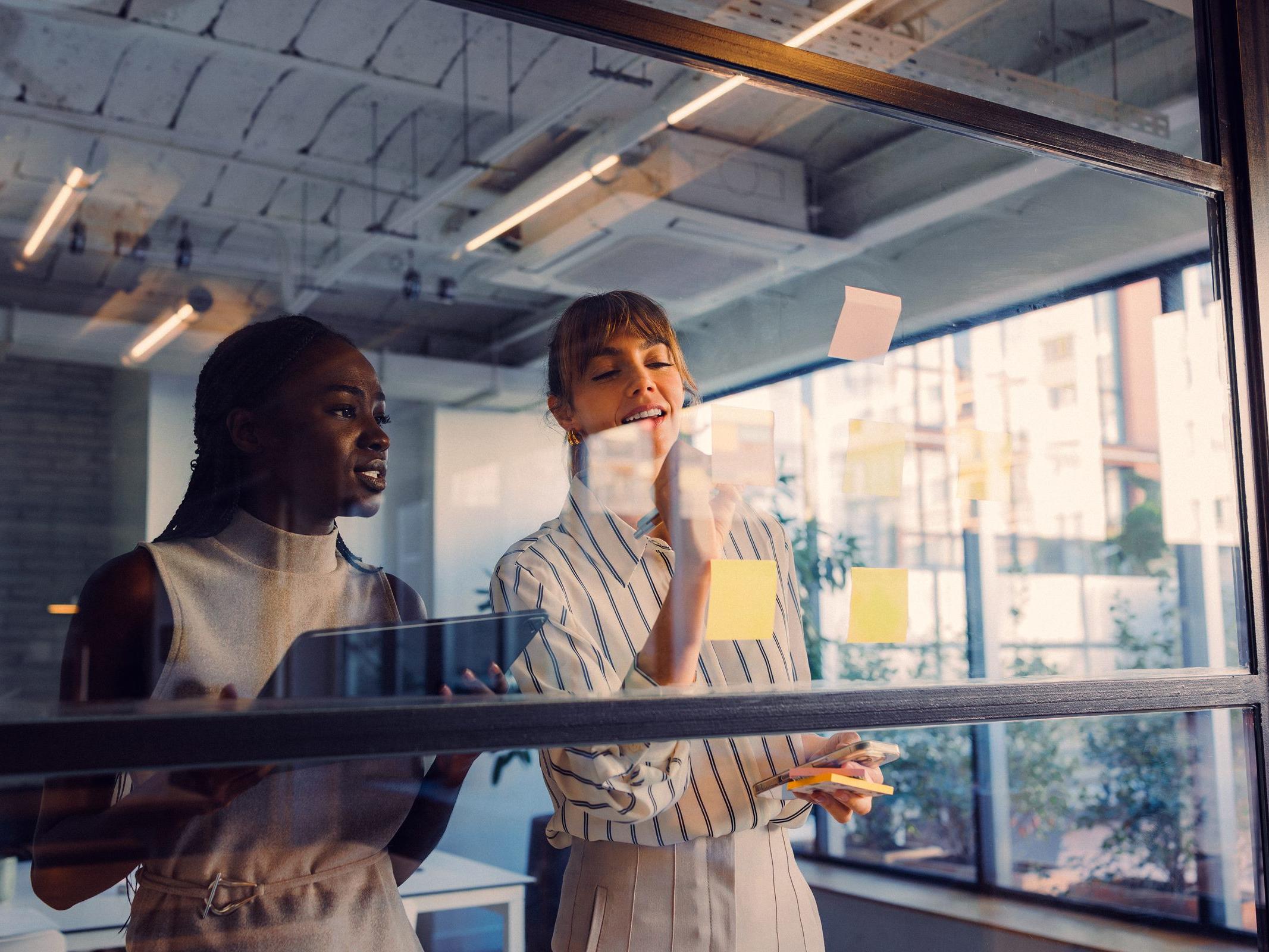 Two colleagues talking beside a glass wall covered in sticky notes
