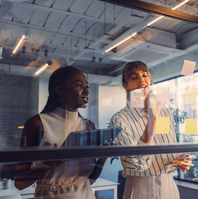 Two woman looking at post its on a transparent wall