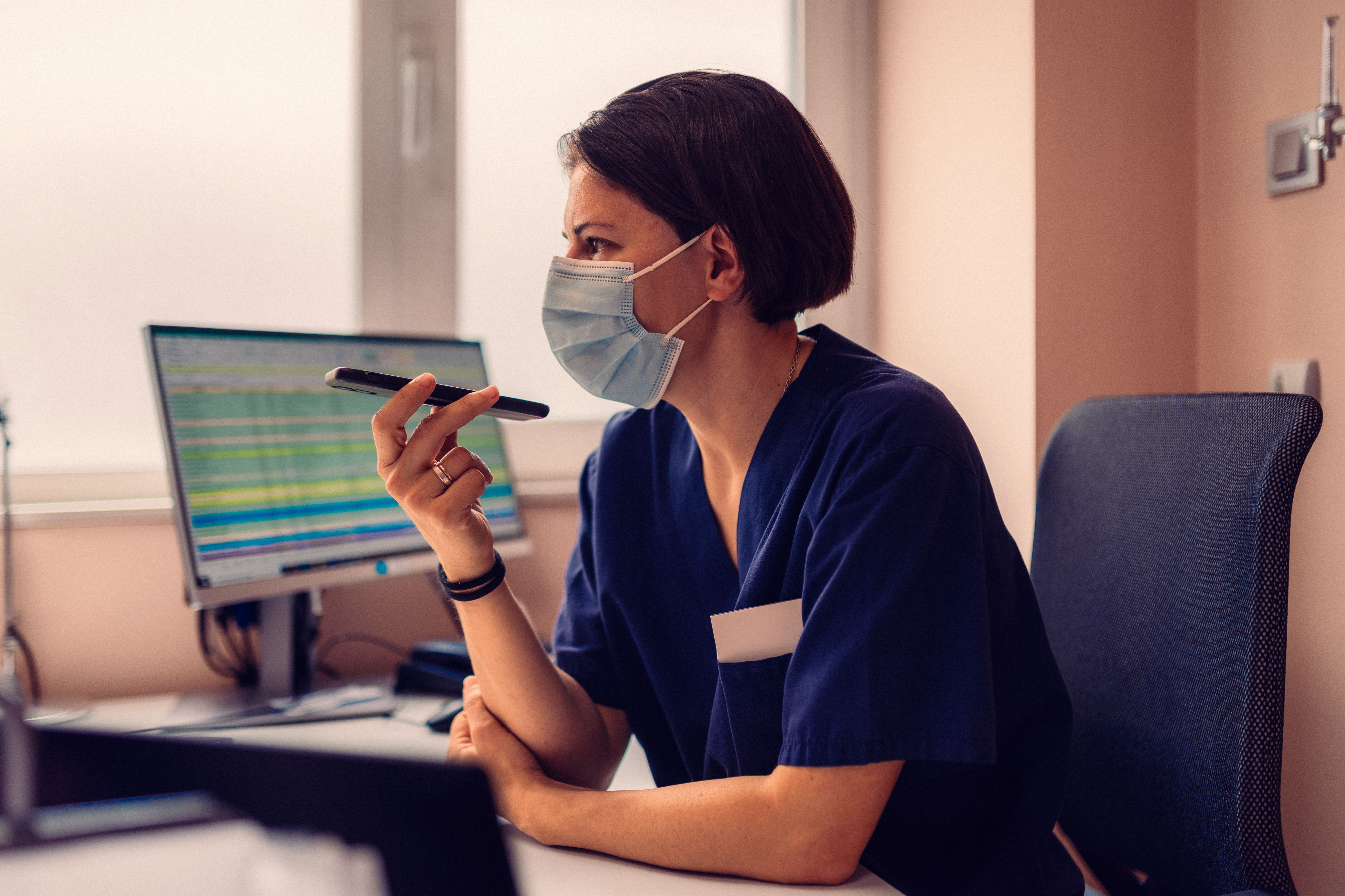 Nurse in a face mask at her computer, holding a pen