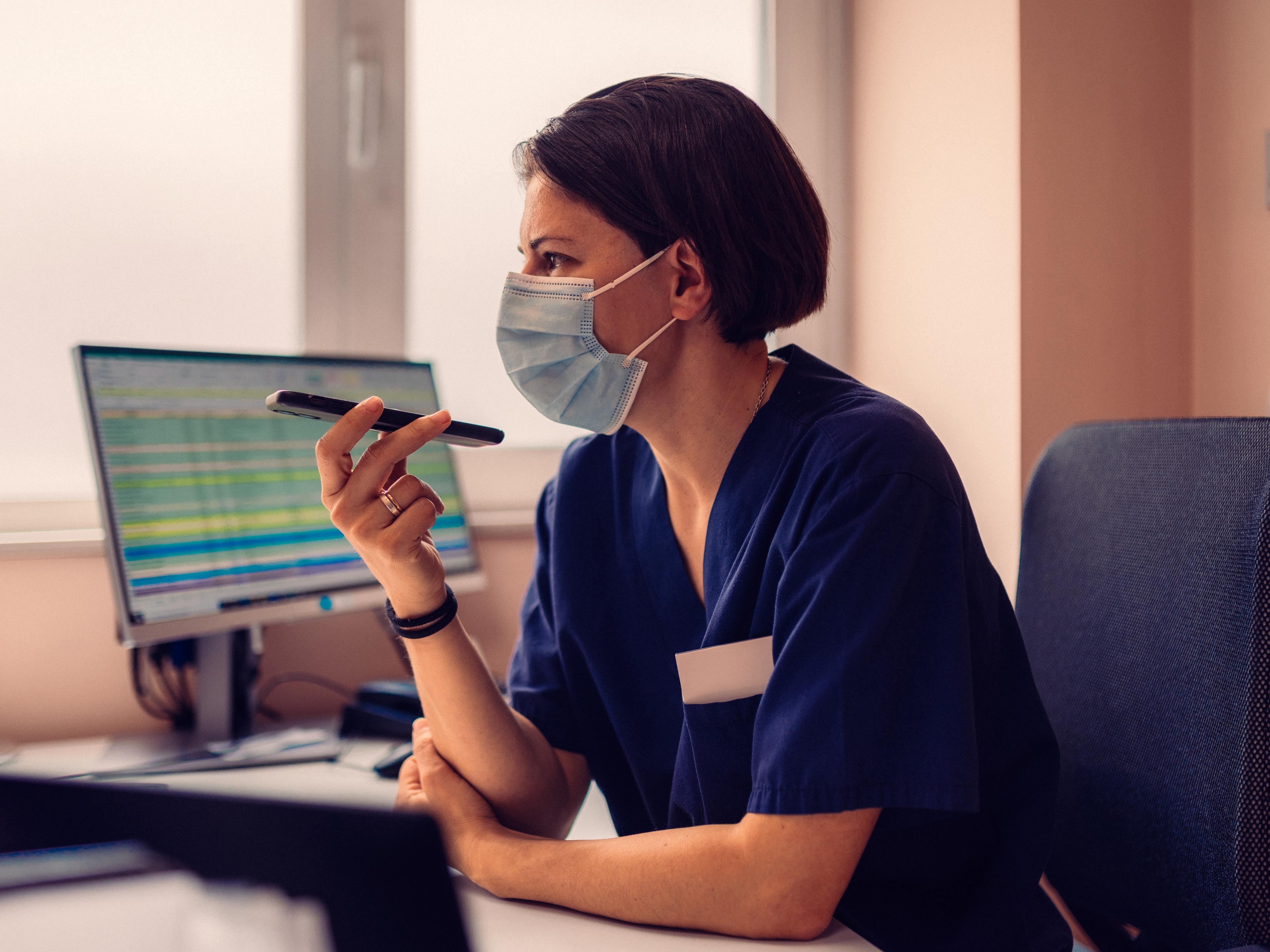 Nurse in a face mask at her computer, holding a pen