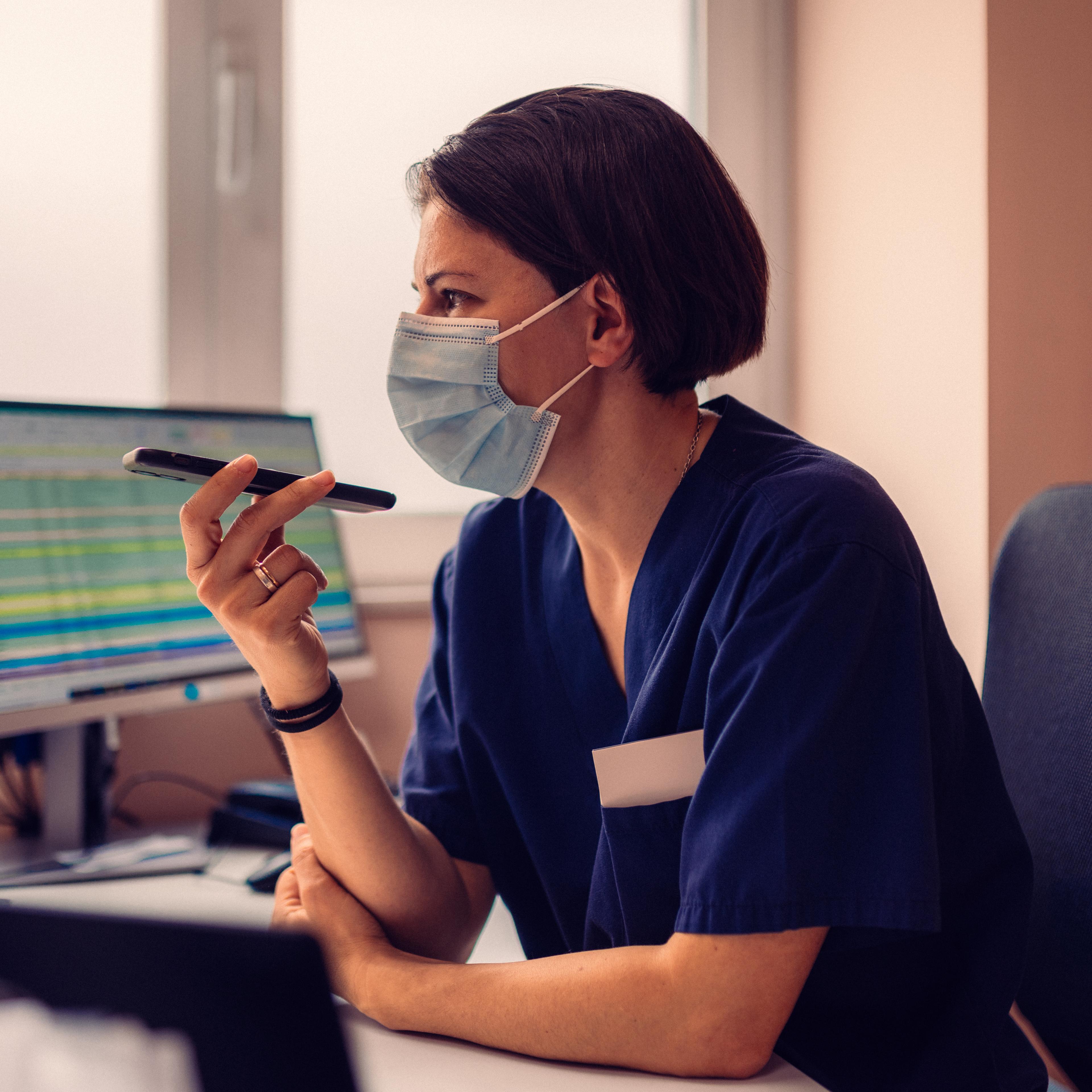 Nurse in a face mask at her computer, holding a pen