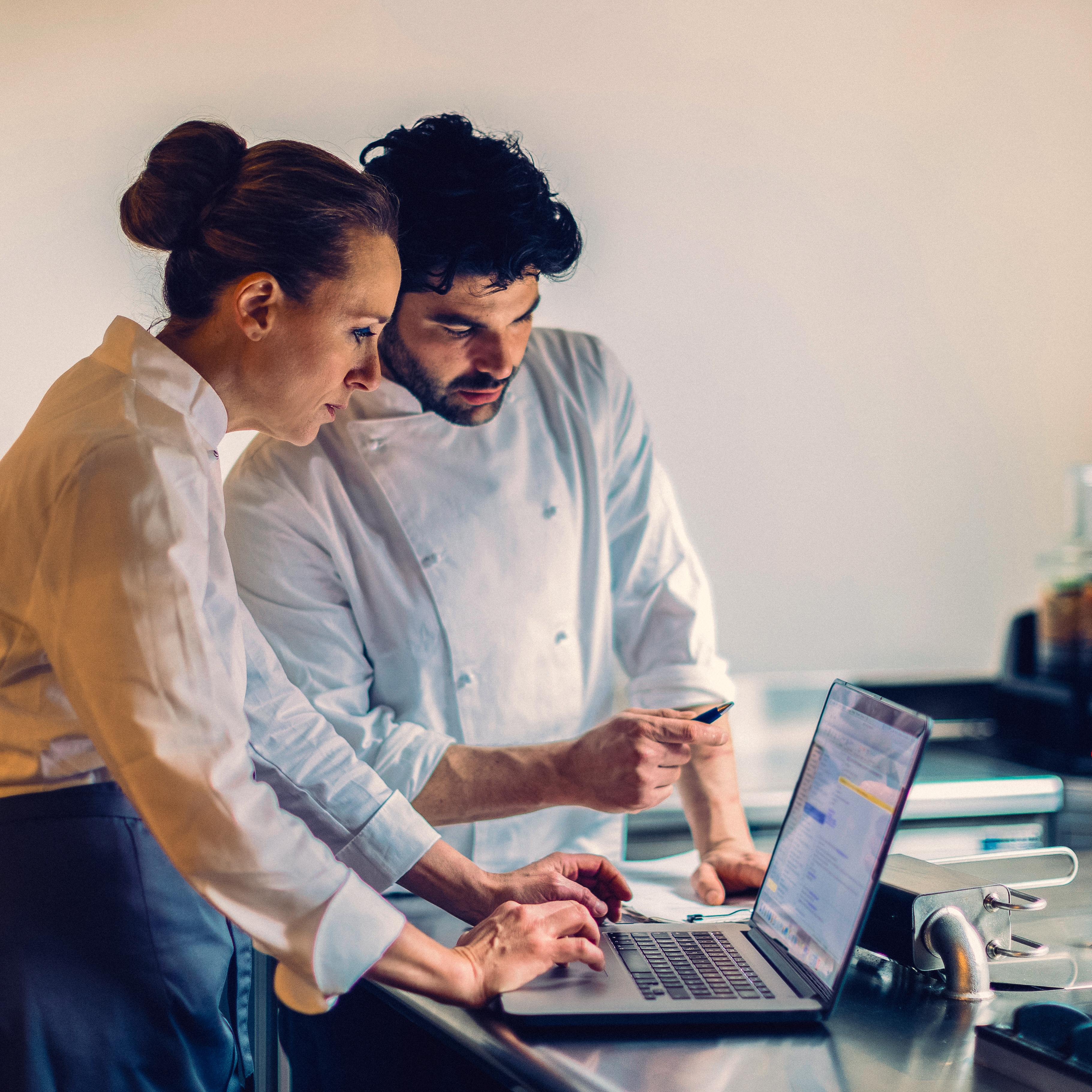 Chef and a colleague checking an order on a laptop in a kitchen