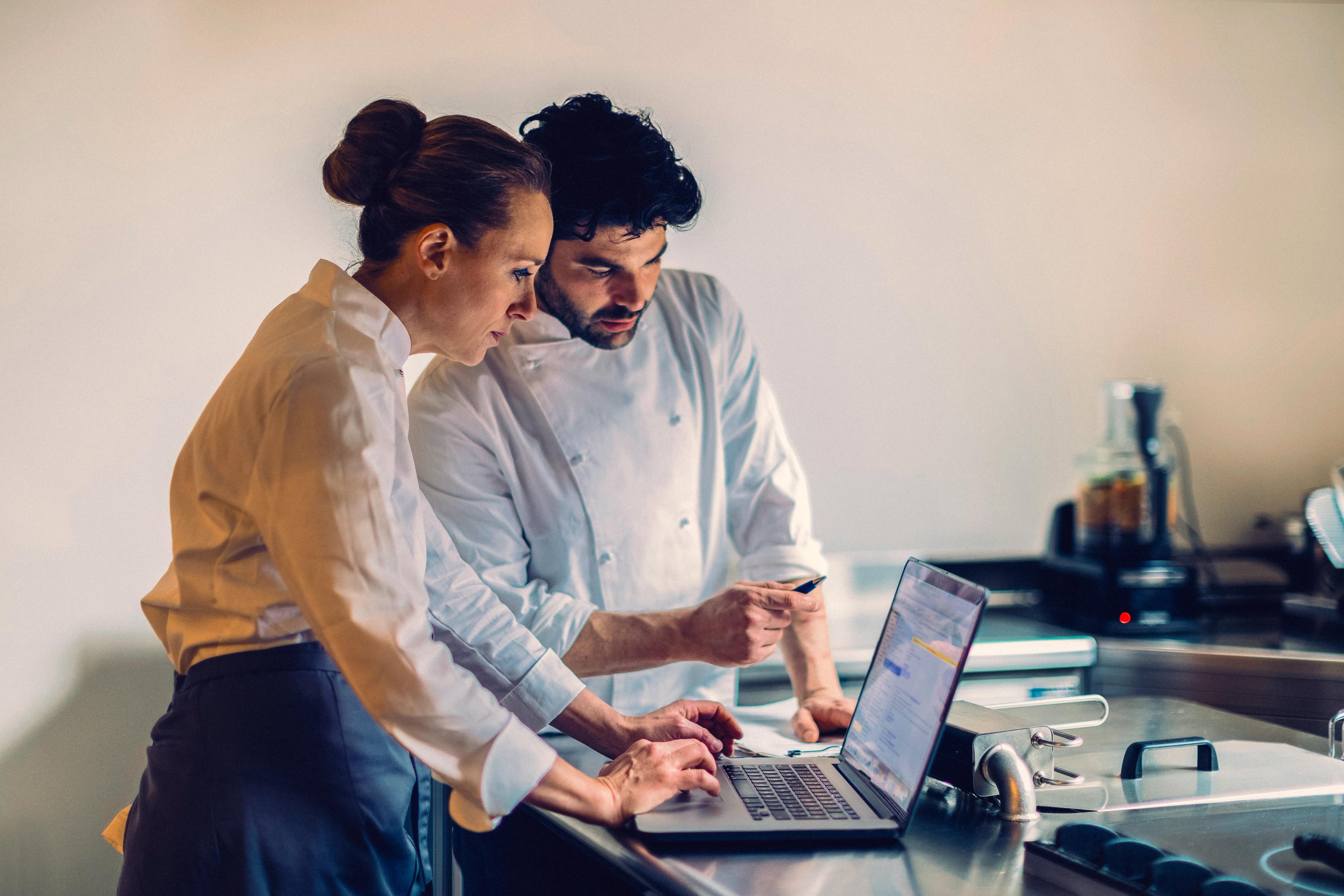 Chef and a colleague checking an order on a laptop in a kitchen