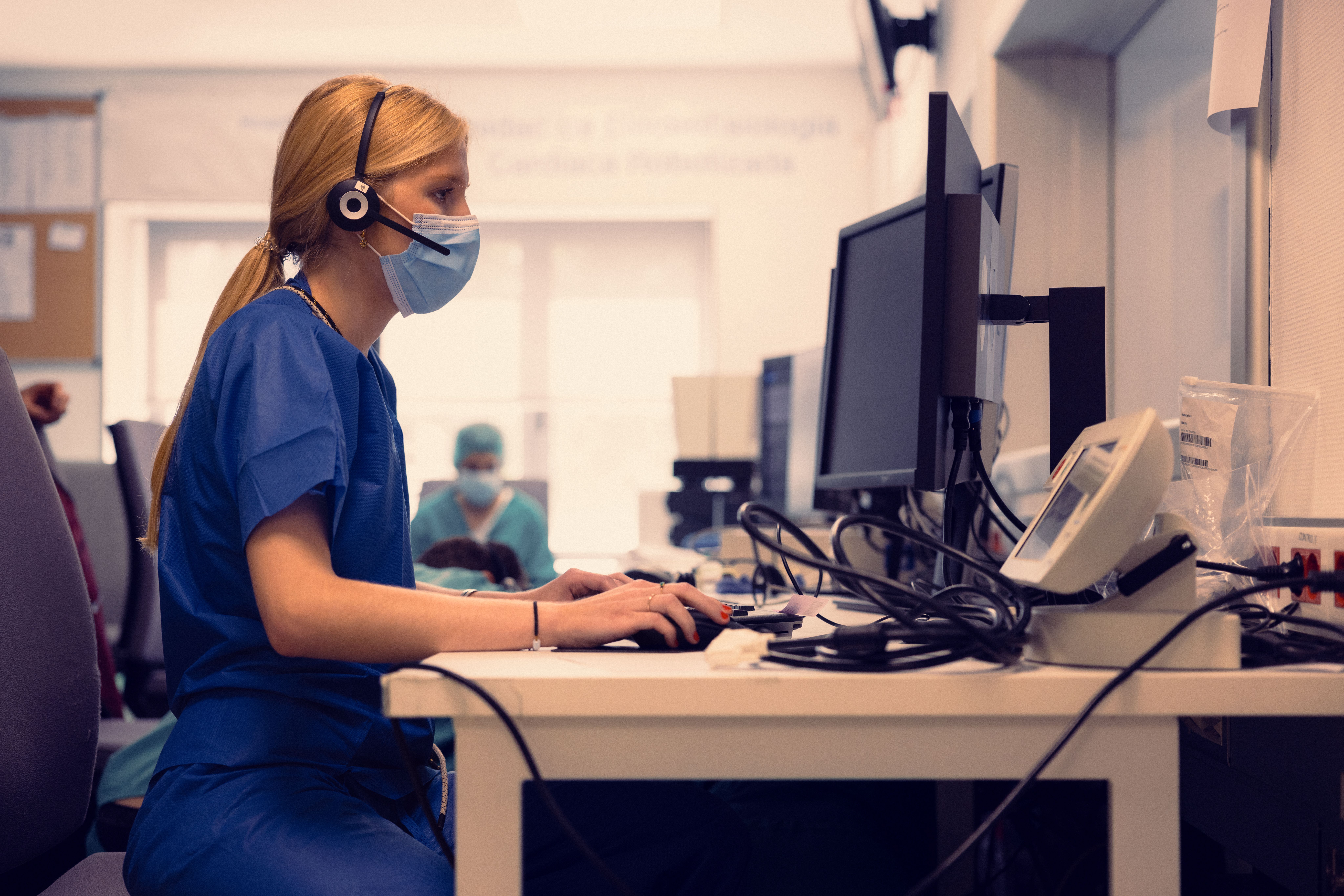Nurse in a headset and face mask typing at a hospital front desk
