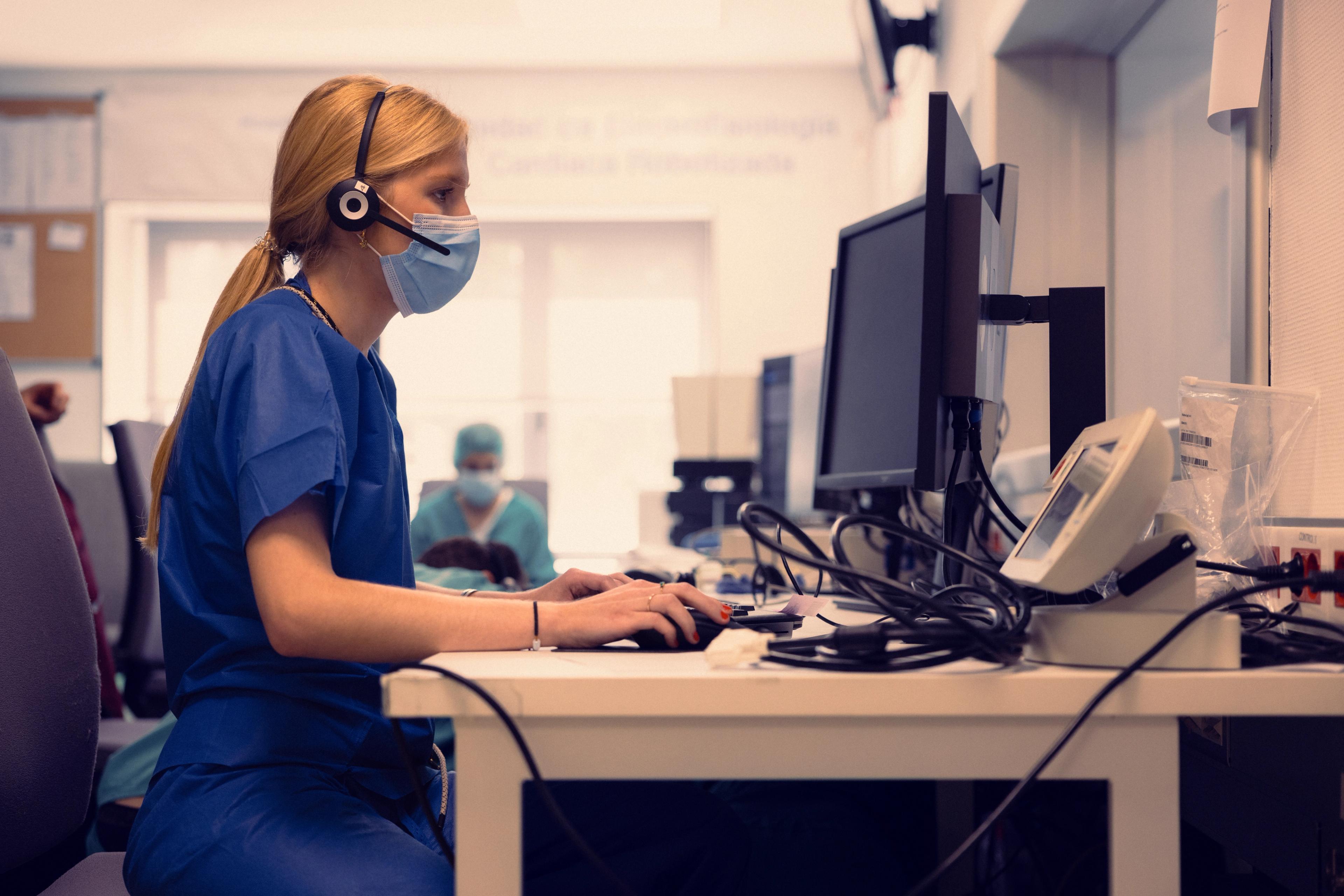 Nurse in a headset and face mask typing at a hospital front desk