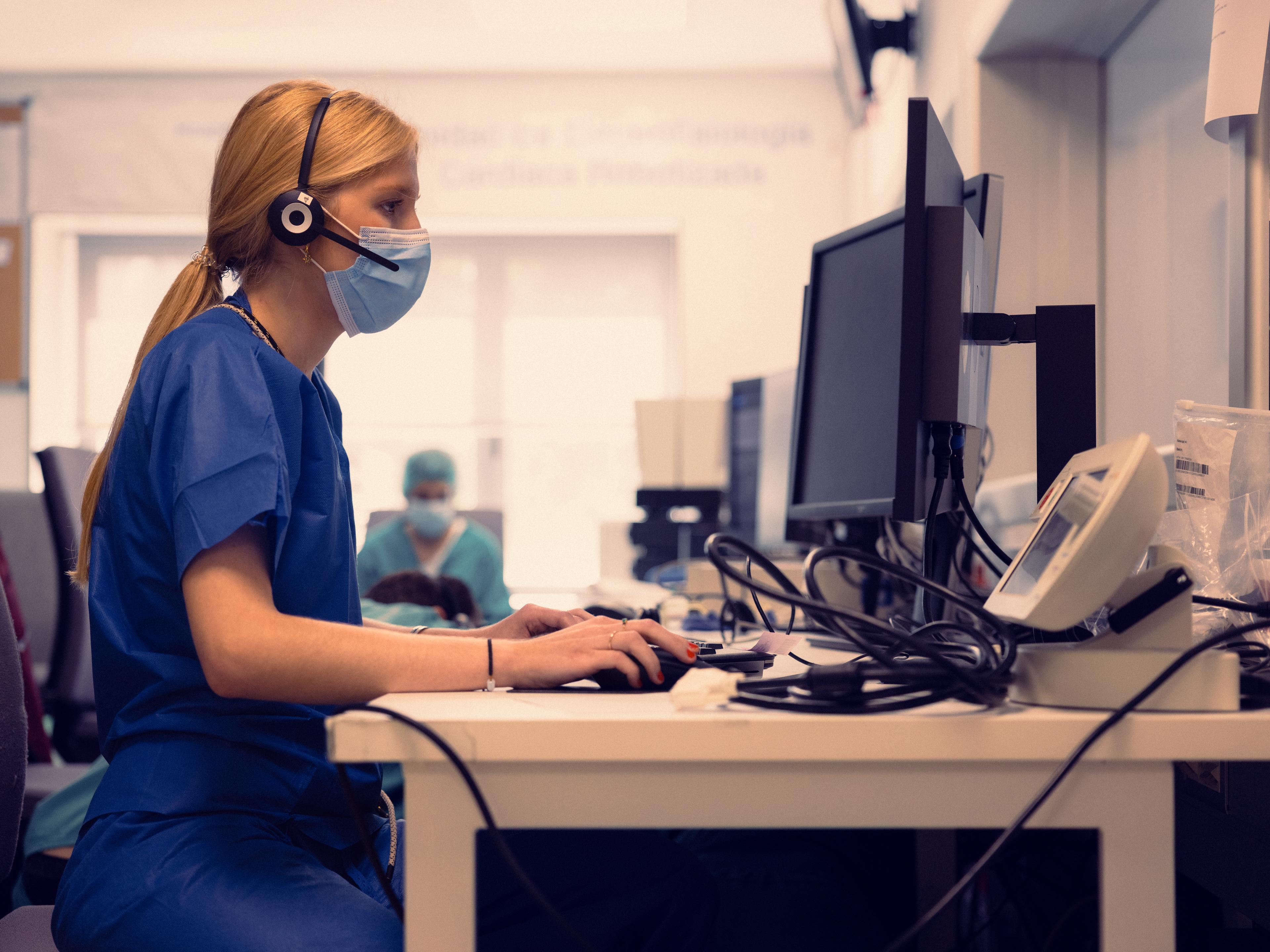 Nurse in a headset and face mask typing at a hospital front desk