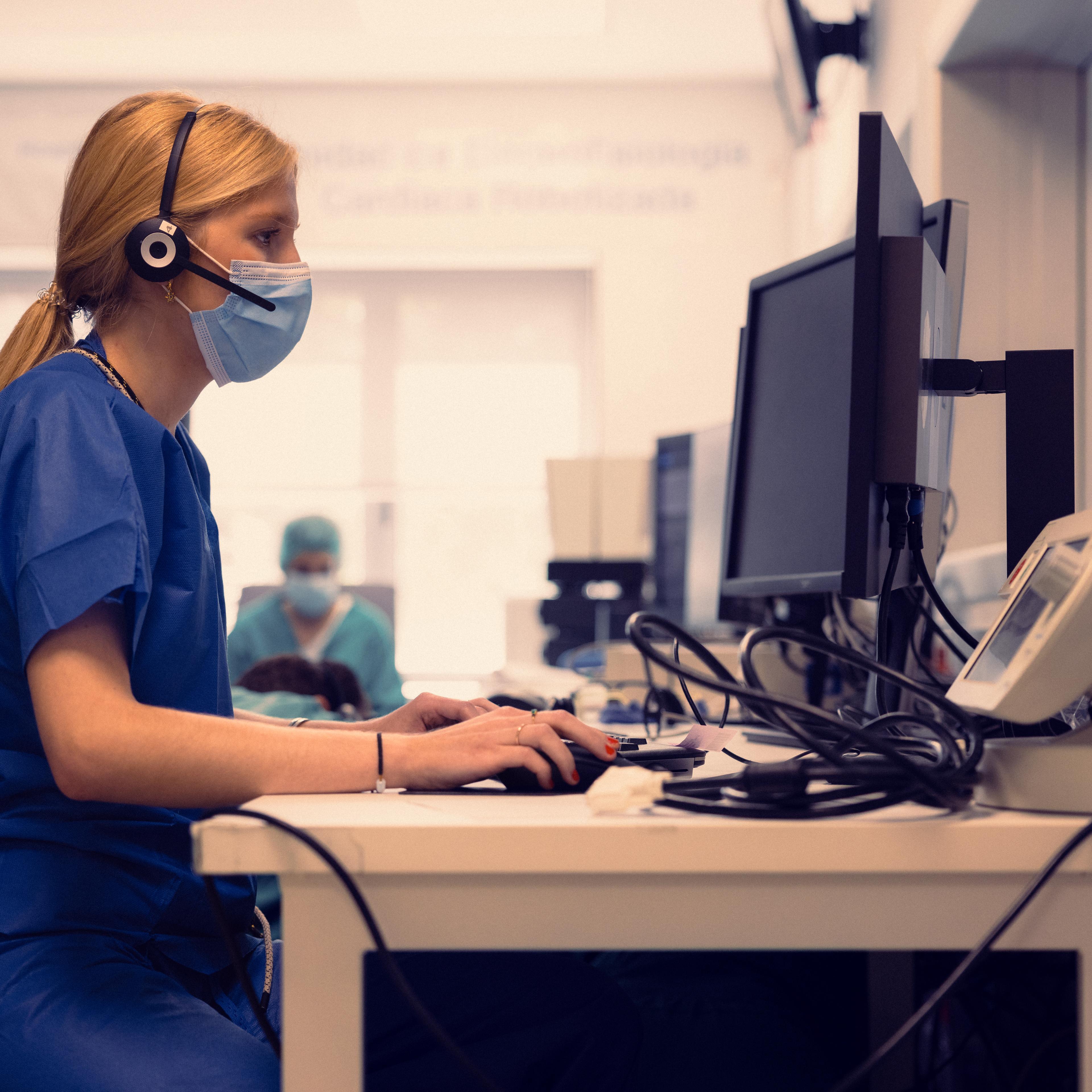 Nurse in a headset and face mask typing at a hospital front desk