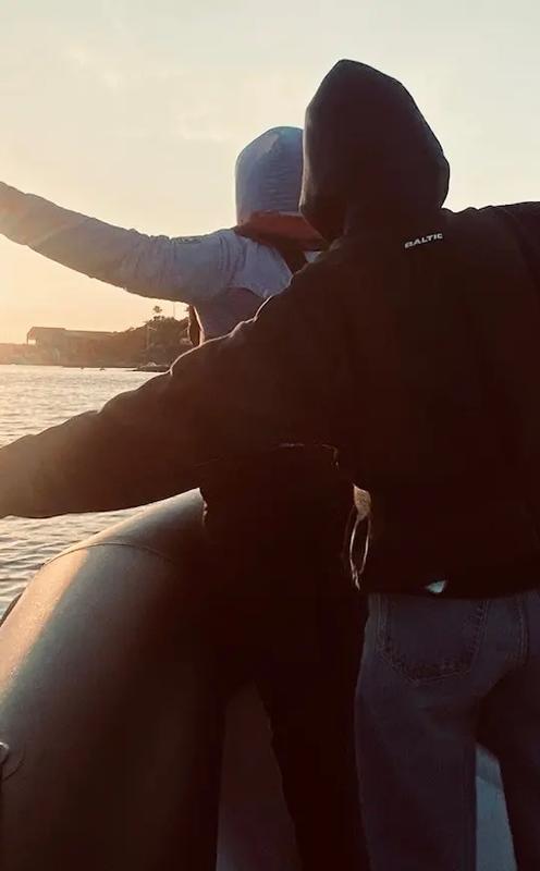 KUP to unge står foran i en båt med armene i været under solnedgang