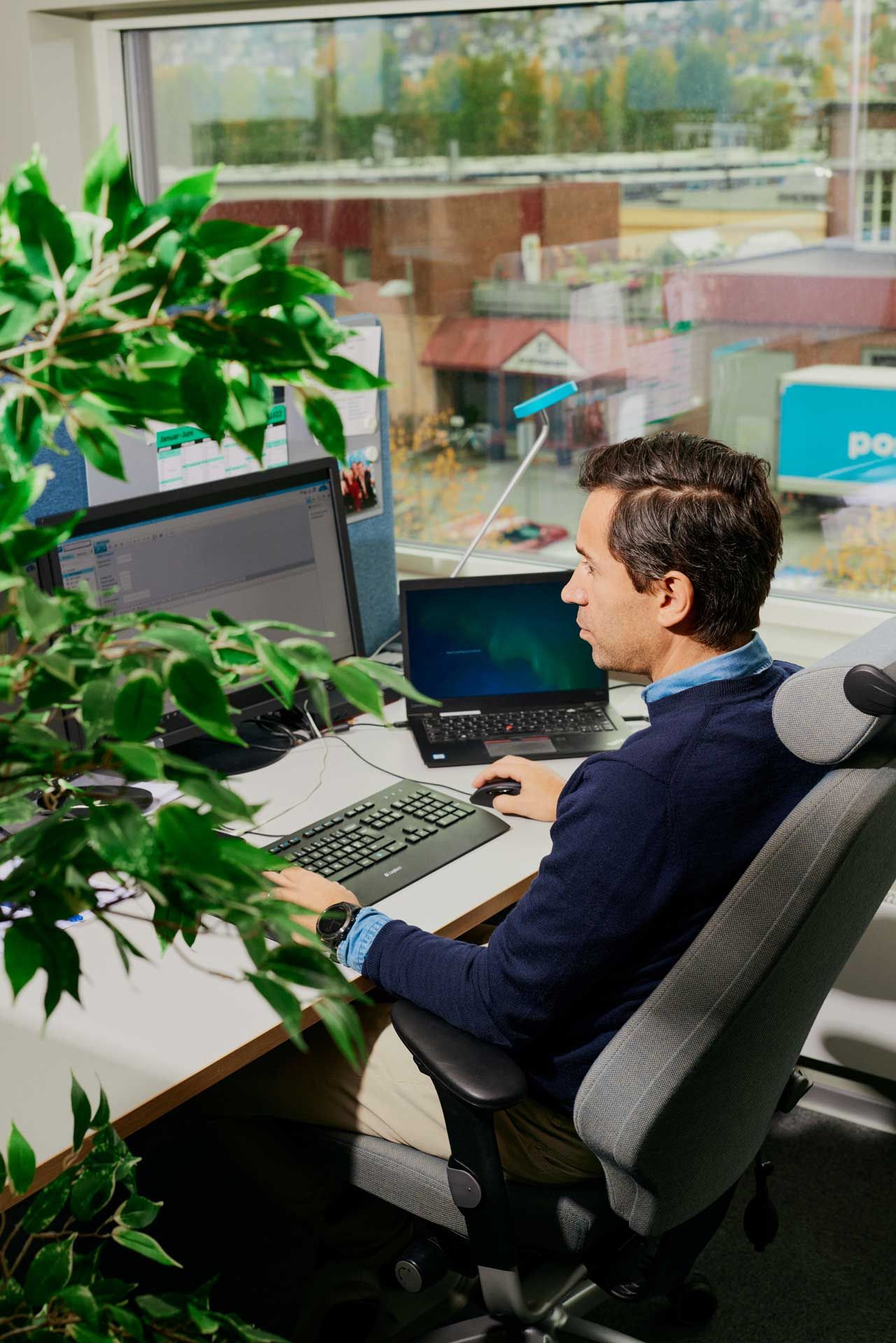 Mann ved pc i kontorlandskap. Foto.