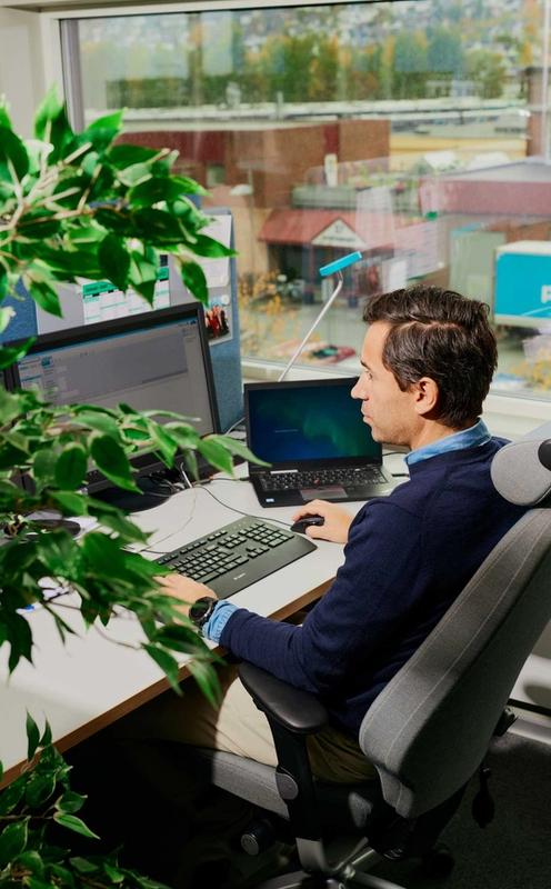 Mann ved pc i kontorlandskap. Foto.