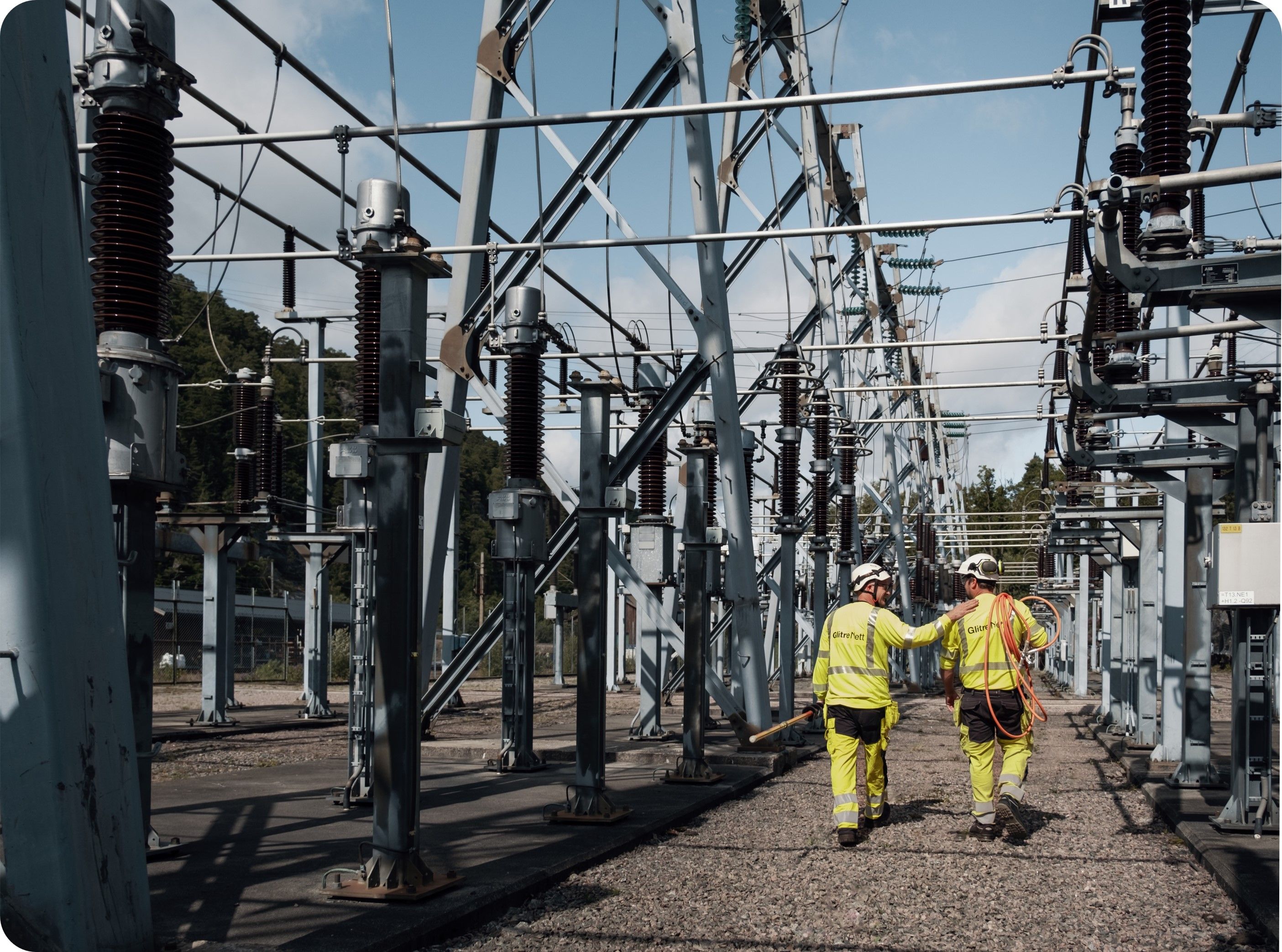 To arbeidsfolk inne i koblingsanlegg. Arbeidsklær. Utendørs.