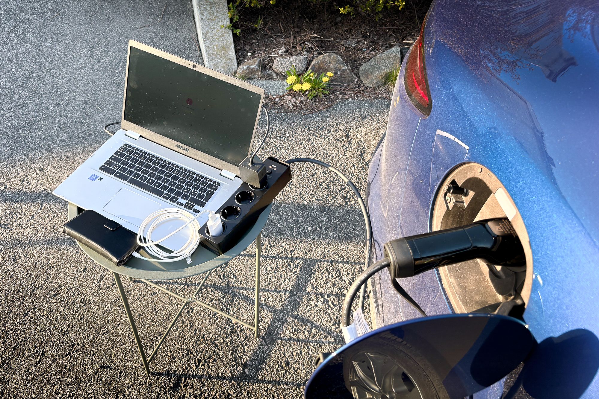 Laptop og mobil som får strøm fra en elbil.