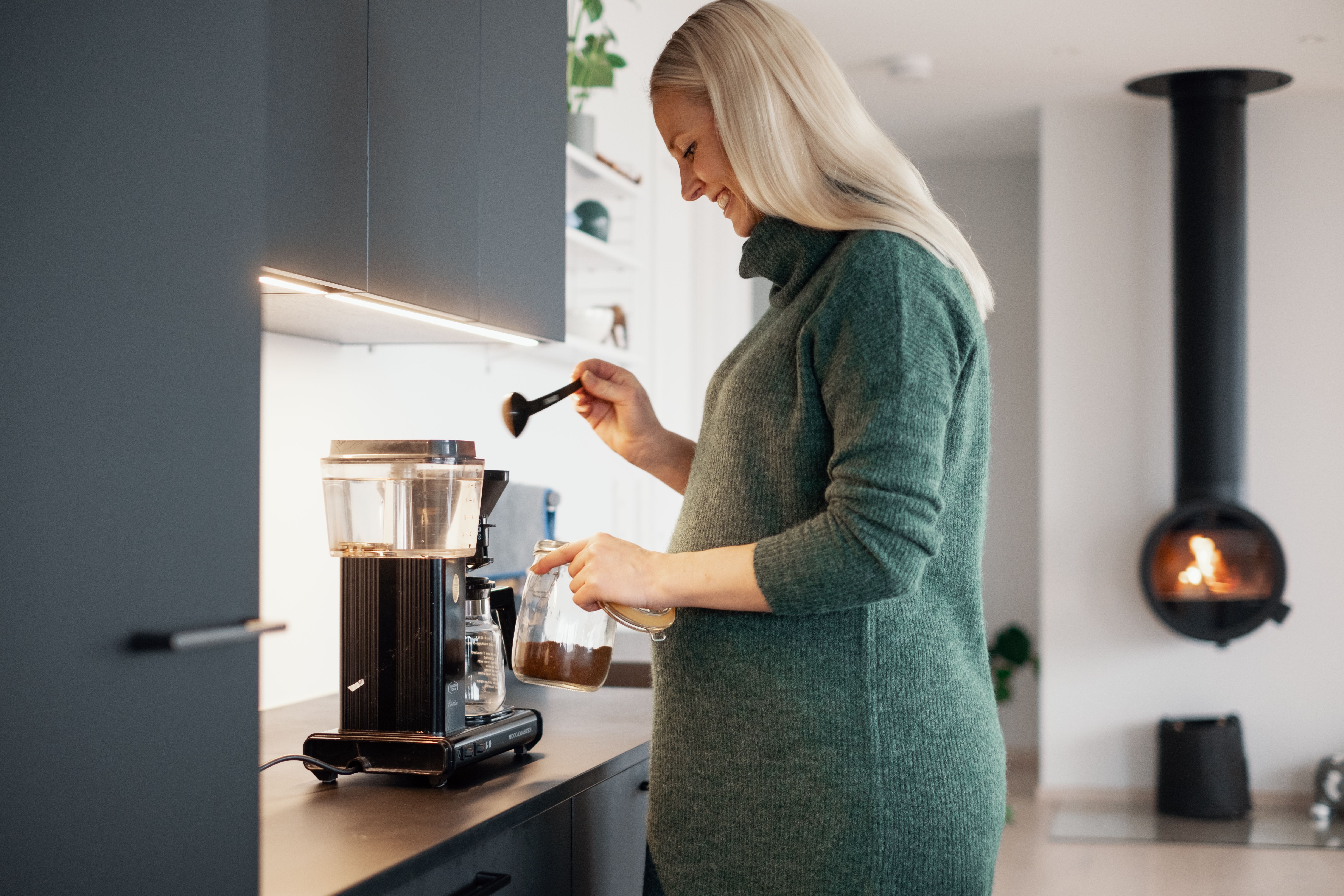 Dame lager kaffe på kjøkkenet og smiler