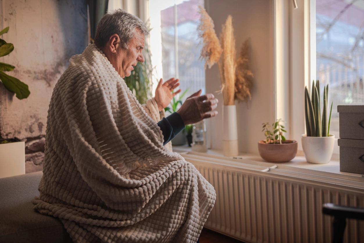 Older man warming himself against heater at home
