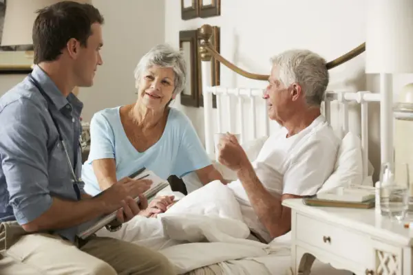Doctor speaking with elderly man in bed and his relative