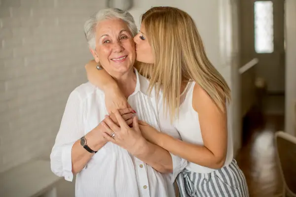 An elderly woman receiving a kiss on the cheek from her granddaughter