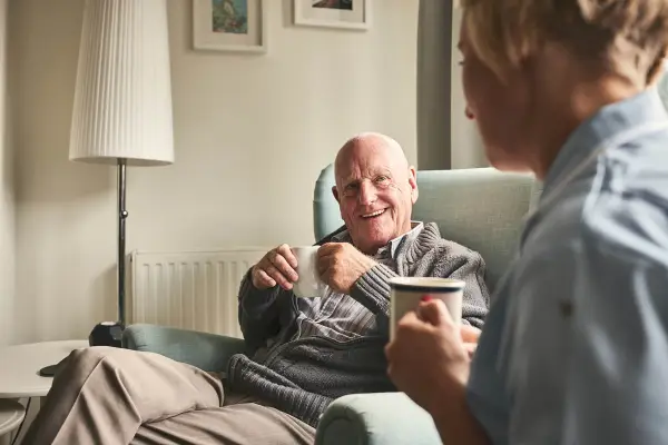 Elderly man drinking a cup of tea with his carer