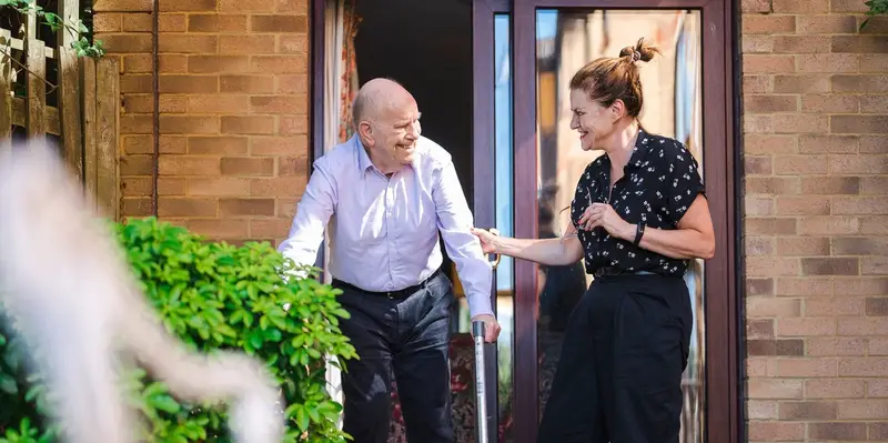 Carer cutting vegetables with an older person watches