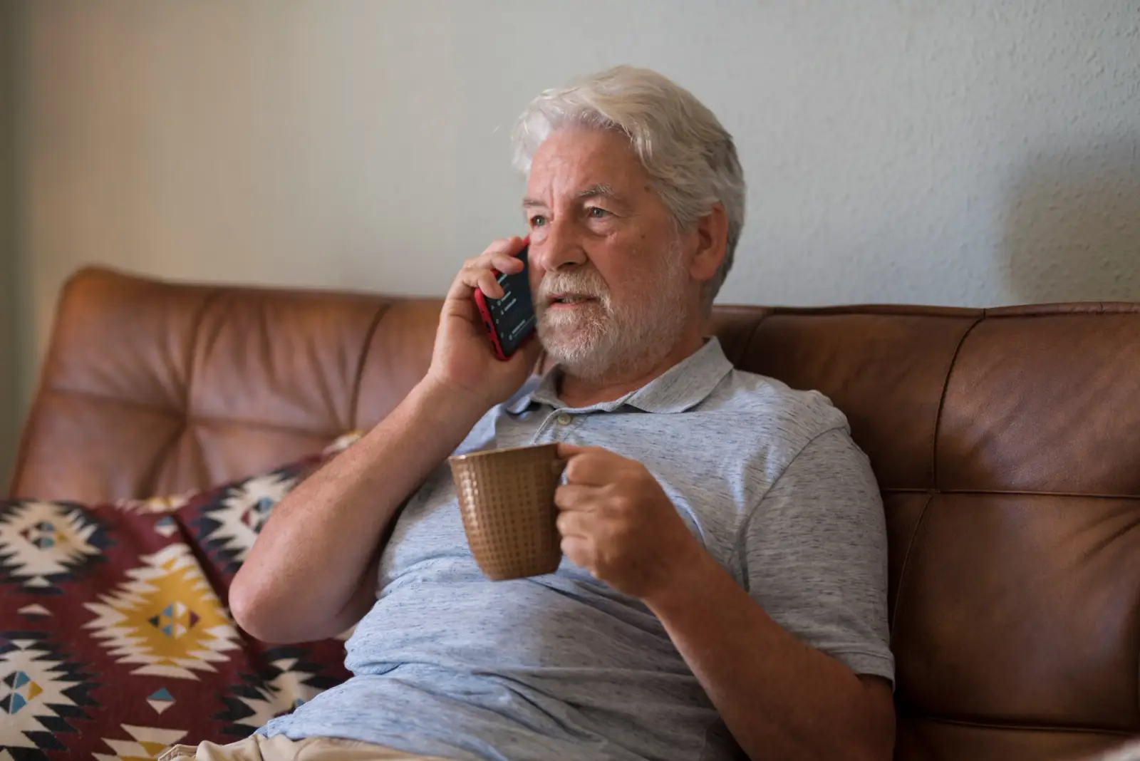 Older man sitting on couch with phone and hot drink
