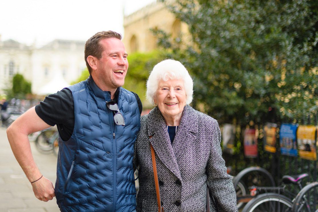 An adult man takes a walk with his elderly mother outside in a quiet town