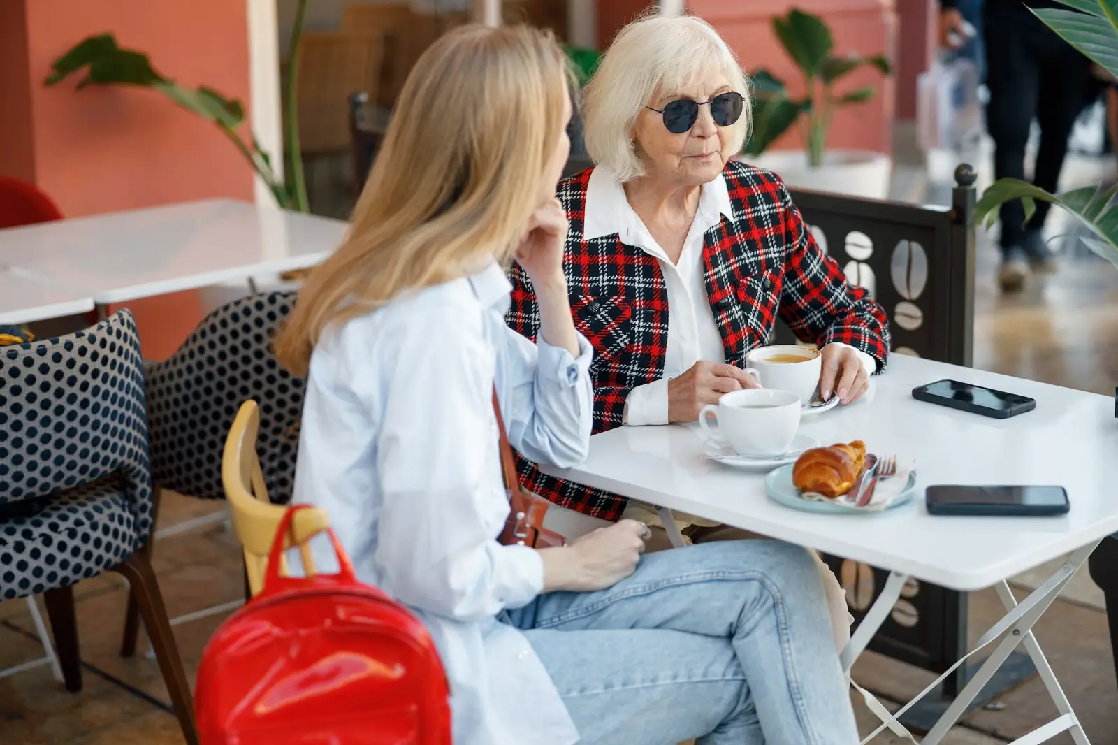 Older woman sits with younger woman outside cafe with coffee