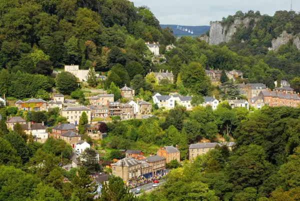Aerial view of a Derbyshire village nestled in a wooded valley, with a cable car and limestone cliffs visible above