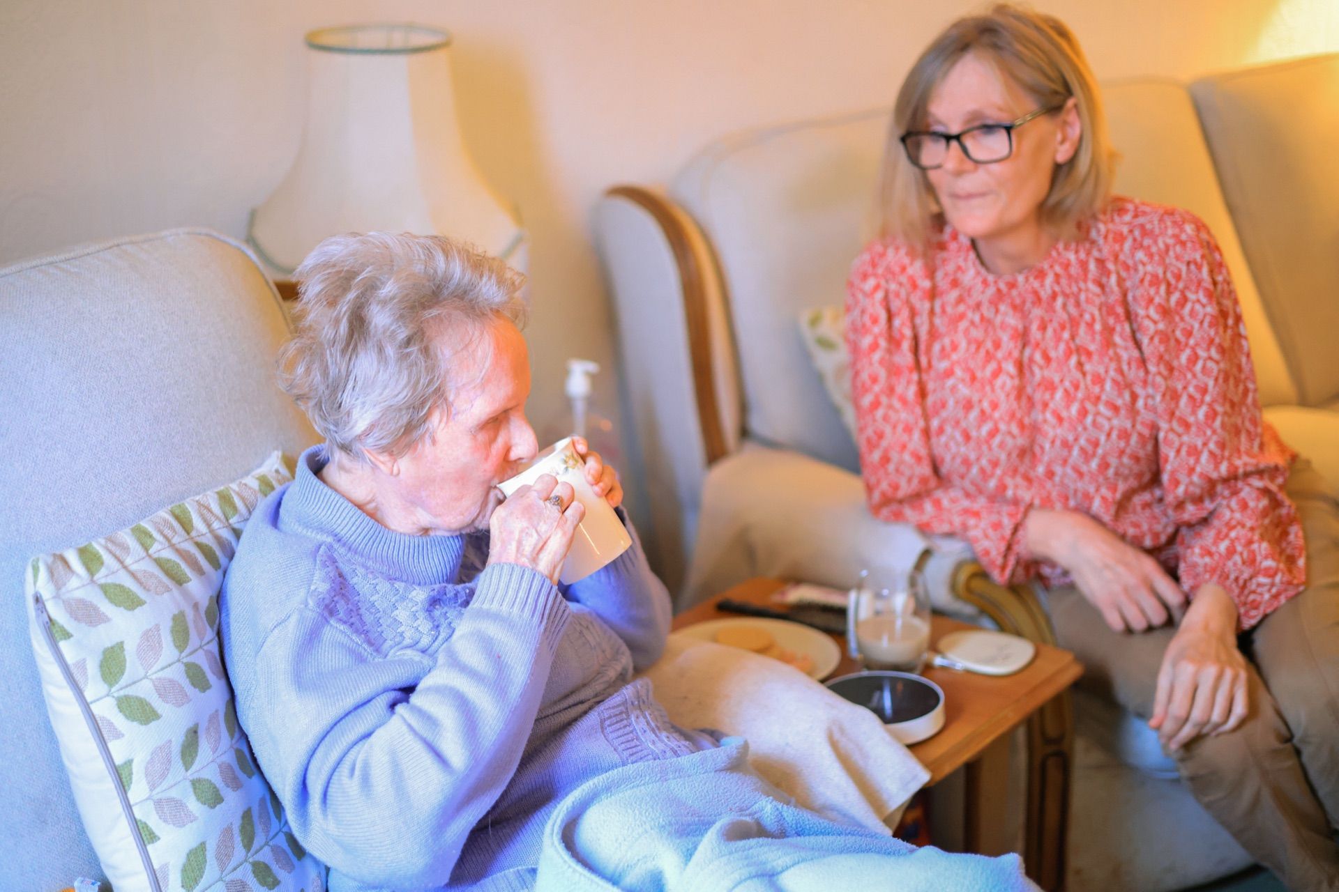 Older woman drinking tea with carer next to her